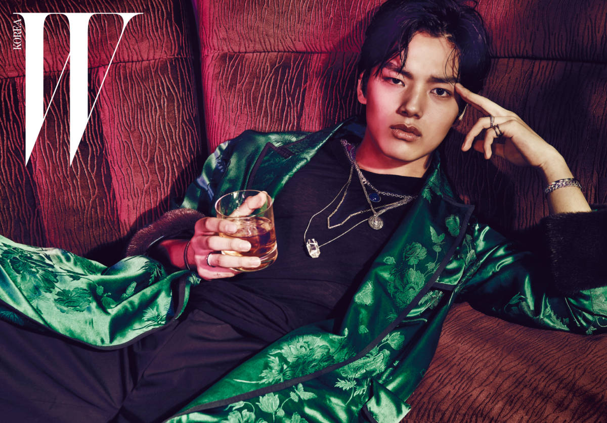 Jin 桌布 壁紙 — 一位時尚年輕男子身穿綠色花卉緞面長袍，手持一杯威士忌，慵懶地躺在紅色紋理沙發上。