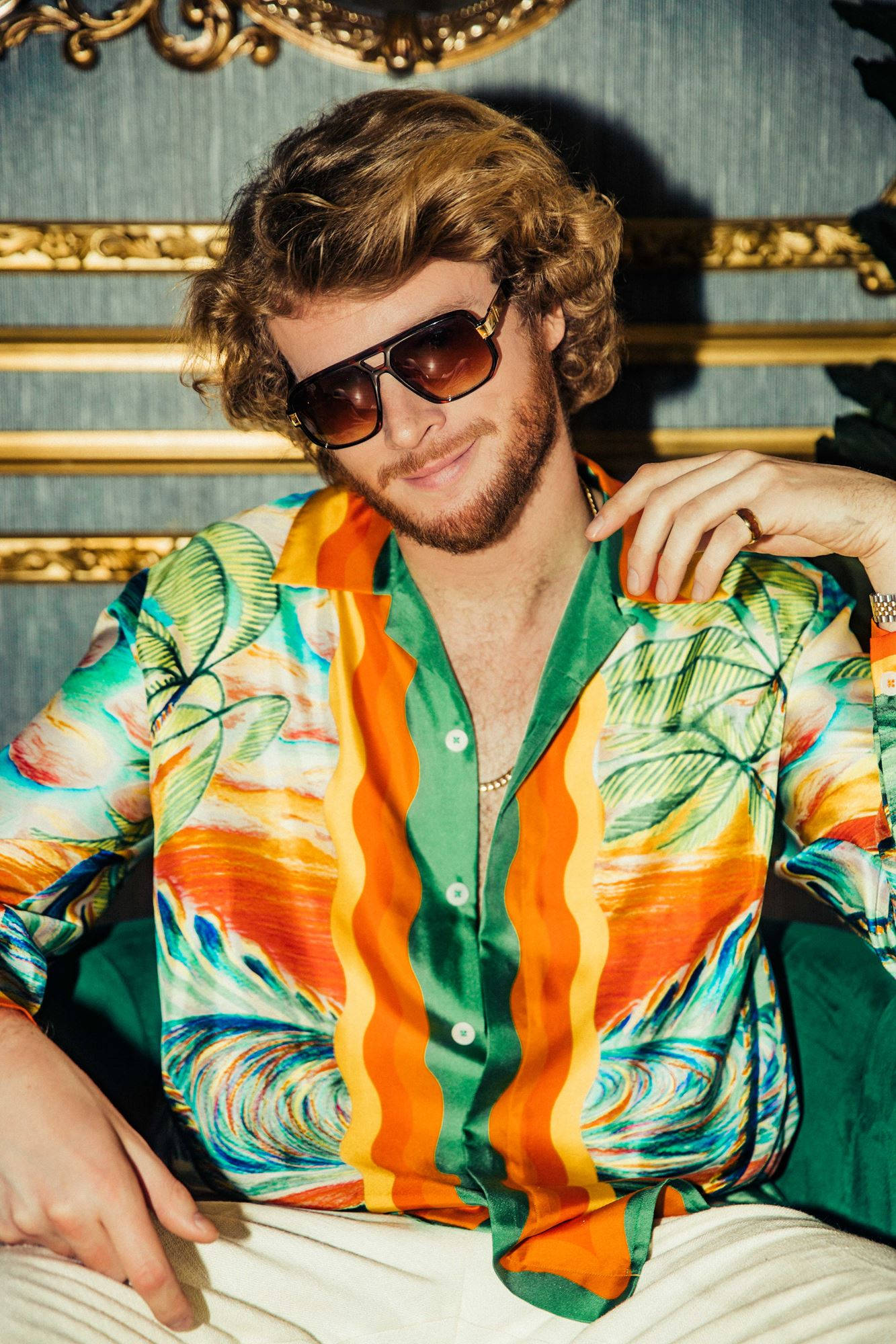 Sunglasses 桌布 壁紙 — 一位時尚男士，捲髮戴太陽眼鏡，身穿鮮豔熱帶襯衫，背景是金色邊框的藍色壁紙。