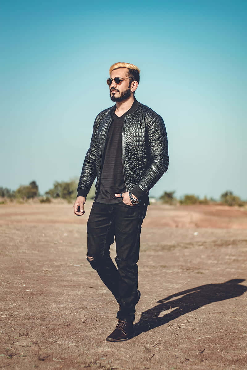 Mens Fashion 桌布 壁紙 — 一位時尚男士，金髮，戴太陽眼鏡，自信地穿著黑色紋理外套，背景是清澈的藍天。