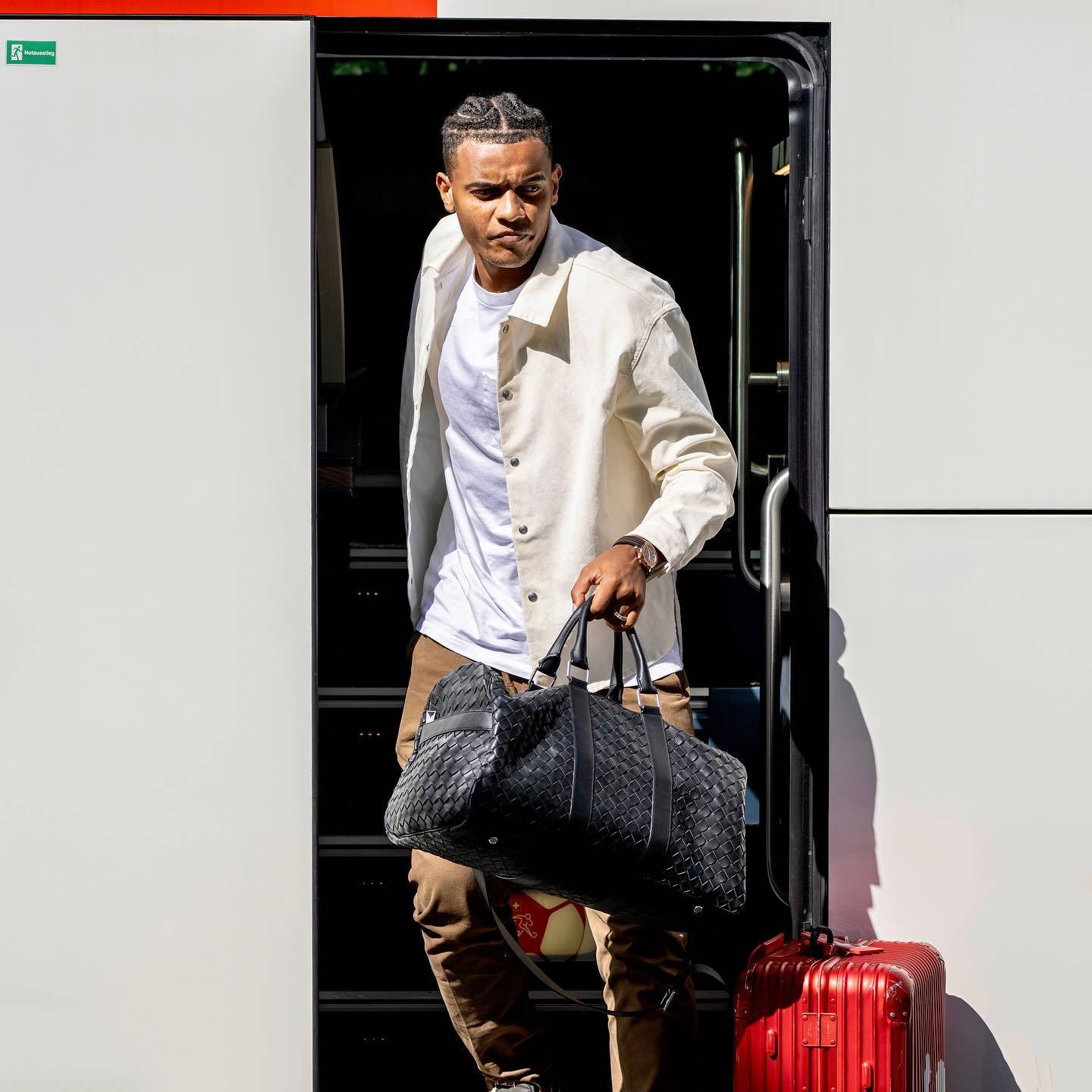 Celebrity 桌布 壁紙 — 一位時尚男士在明亮的陽光下拿著黑色編織袋和紅色行李箱步出巴士。