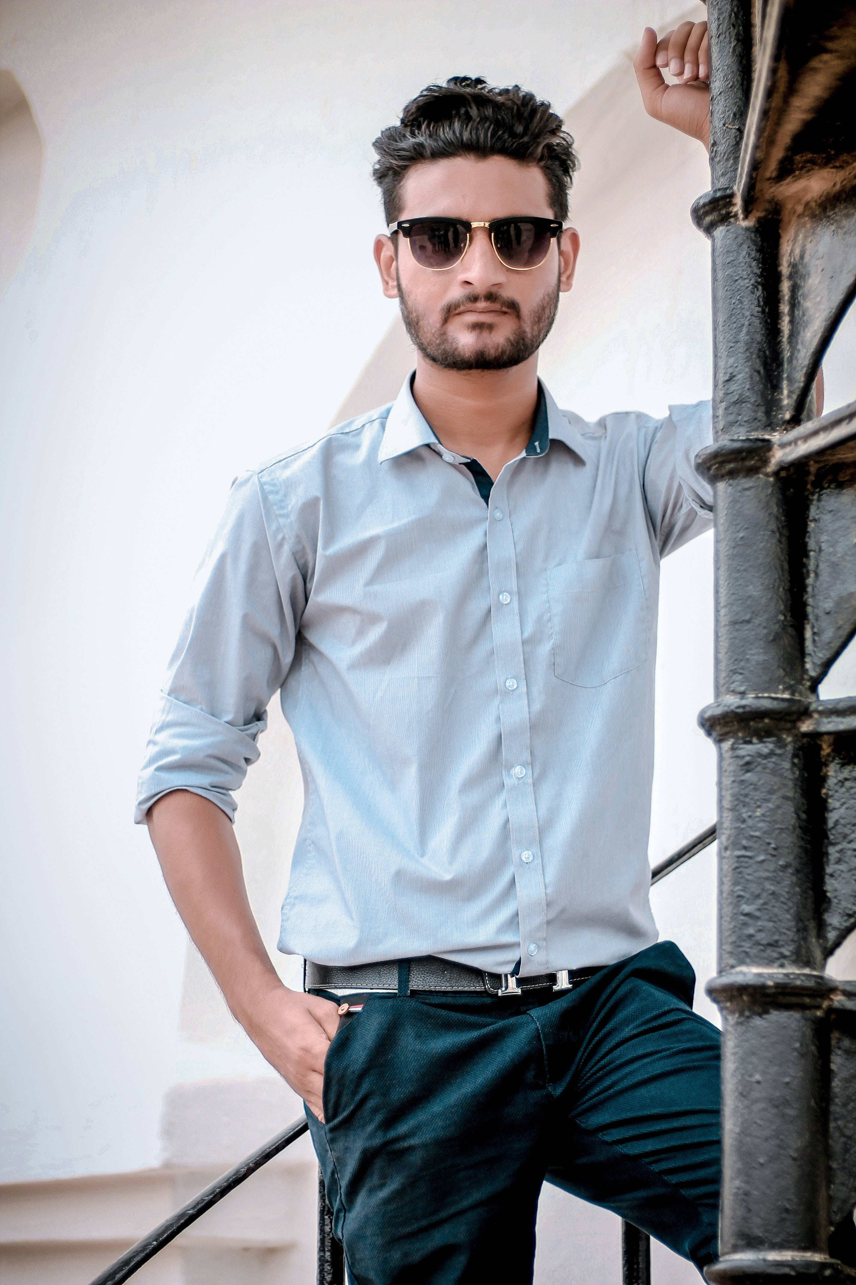 male model 桌布 壁紙 — 一位時尚男士戴著太陽眼鏡，自信地靠在白色樓梯旁的黑色金屬欄杆上。