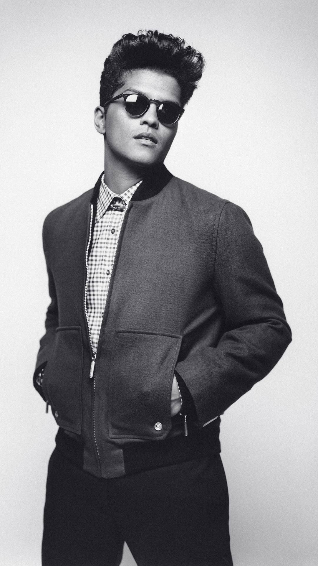 Bruno Mars 桌布 壁紙 — 一位時尚男士戴著太陽眼鏡和飛行員夾克，在單色背景下自信地擺姿勢。