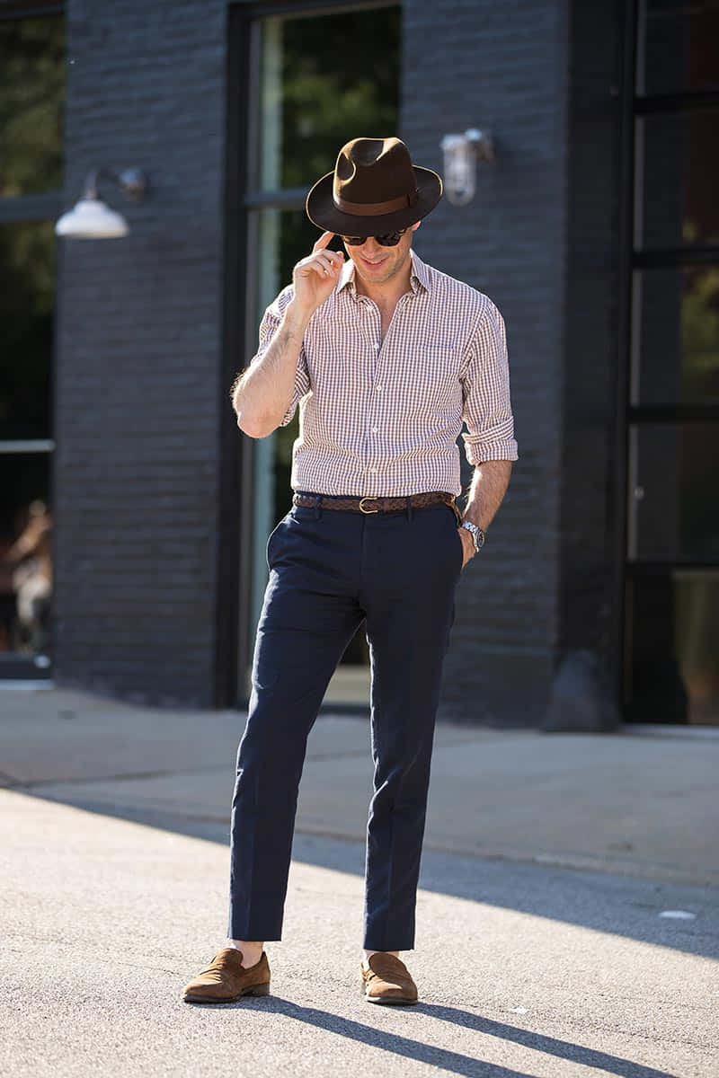 Mens Fashion 桌布 壁紙 — 一位時尚男士戴著棕色軟呢帽和格子襯衫，自信地站在陽光普照的城市人行道上。