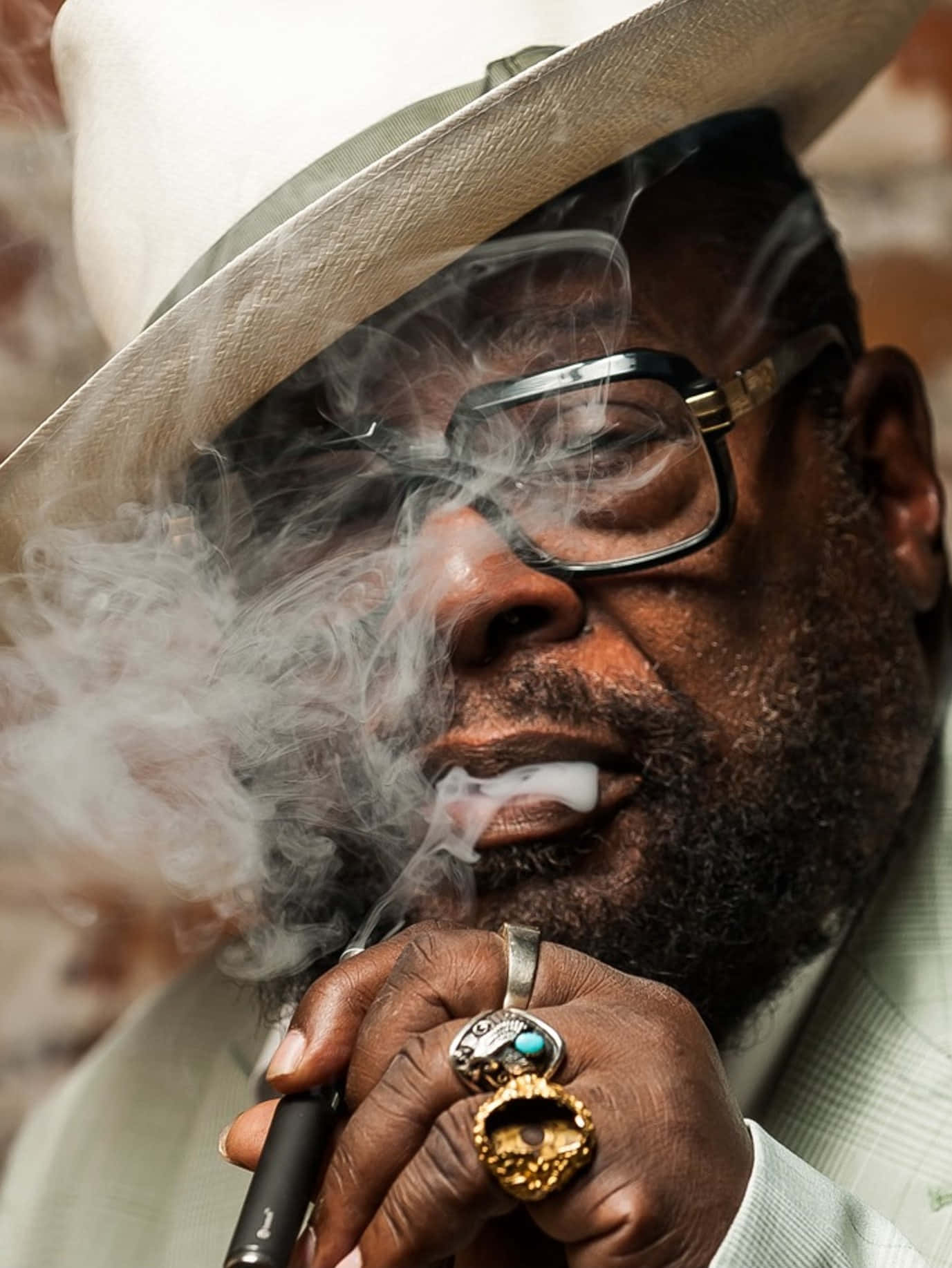 Legend 桌布 壁紙 — 一位時尚男士戴著白色帽子和眼鏡，手持電子煙筆呼出煙霧的特寫肖像。