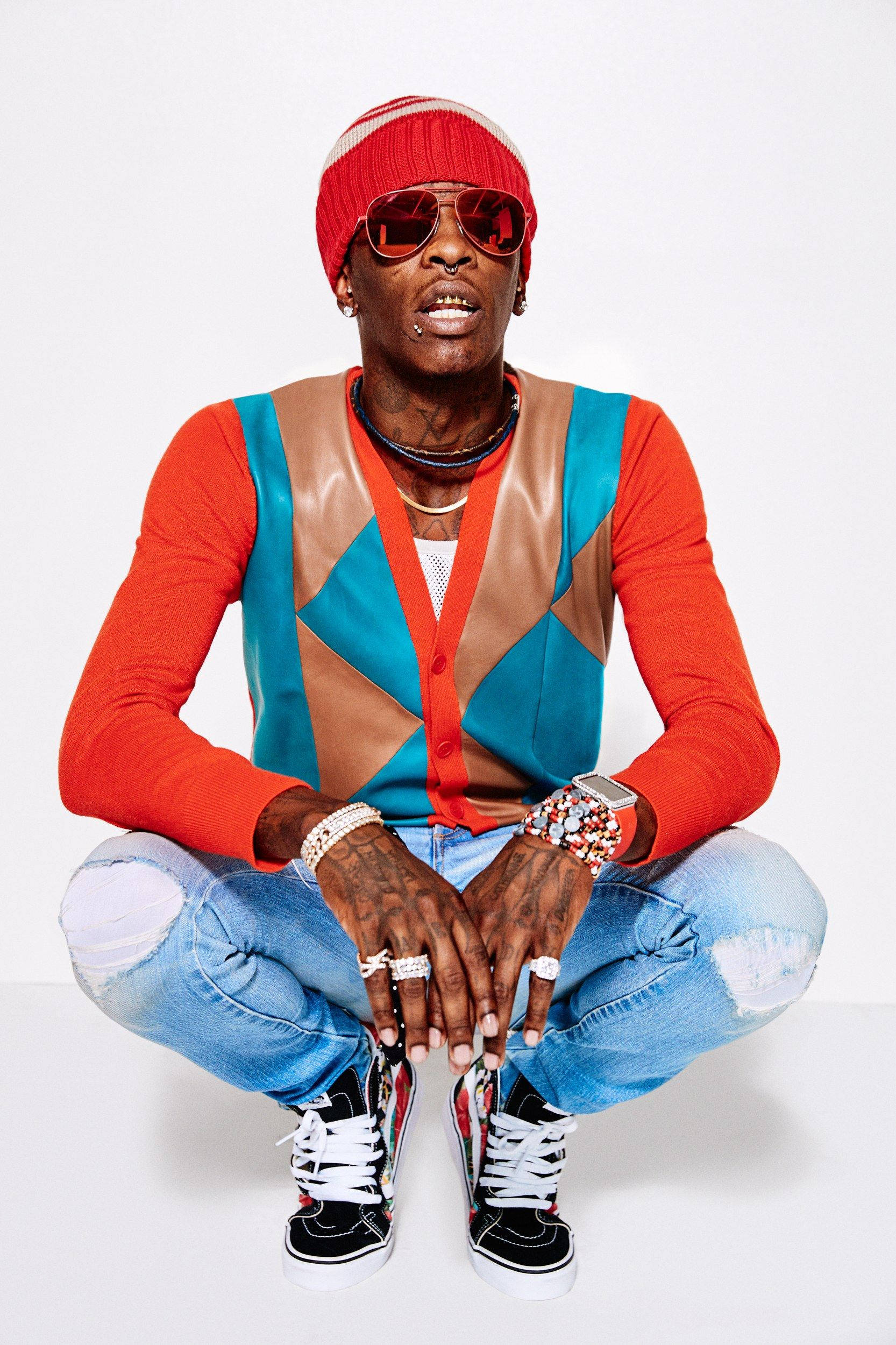 Thug 桌布 壁紙 — 一位時尚男士戴著紅色太陽眼鏡和一件大膽的幾何圖案背心，盤腿坐在純白色背景前。