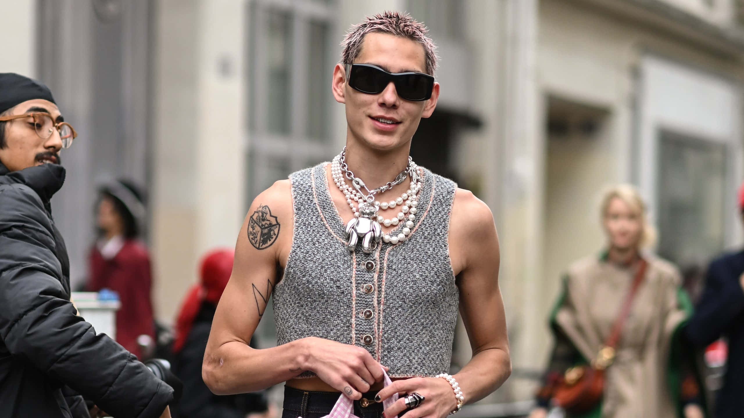 Man 桌布 壁紙 — 一位時尚男士梳著刺蝟頭、戴著太陽眼鏡，穿著層疊珍珠項鍊和質感無袖上衣，走在城市街道上。