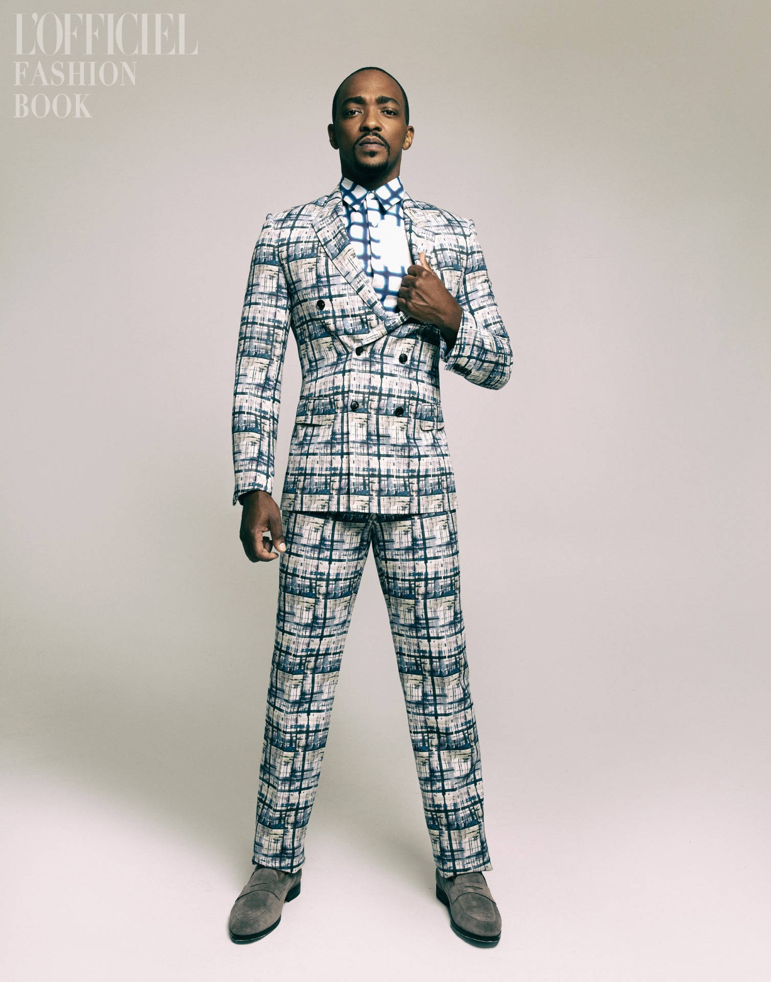 Anthony Mackie 桌布 壁紙 — 一位時尚男士穿著大膽的藍白格紋西裝，自信地站在簡約的攝影棚背景前。