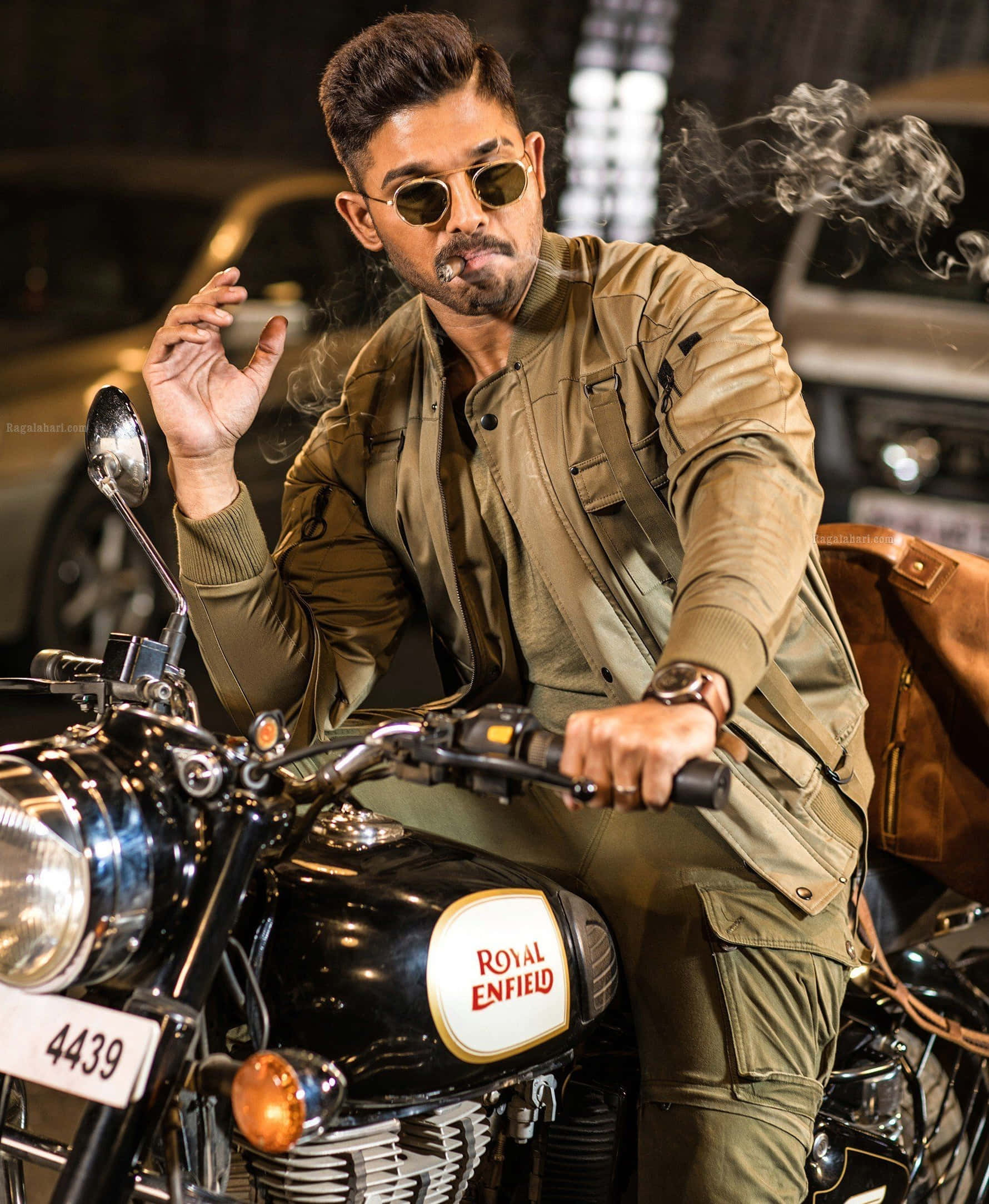 Allu Arjun 桌布 壁紙 — 一位時尚男士穿著棕褐色外套和太陽眼鏡，晚上坐在黑色Royal Enfield機車上抽煙。