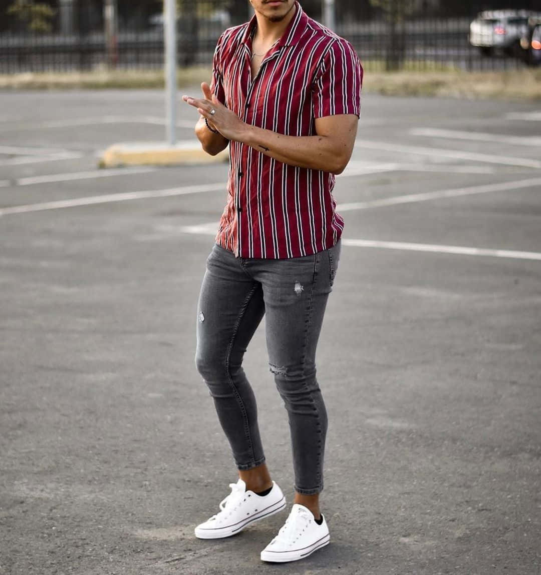 clothing 桌布 壁紙 — 一位時尚男士穿著紅色條紋襯衫和破洞牛仔褲，自信地站在空蕩蕩的停車場，腳穿白色運動鞋。