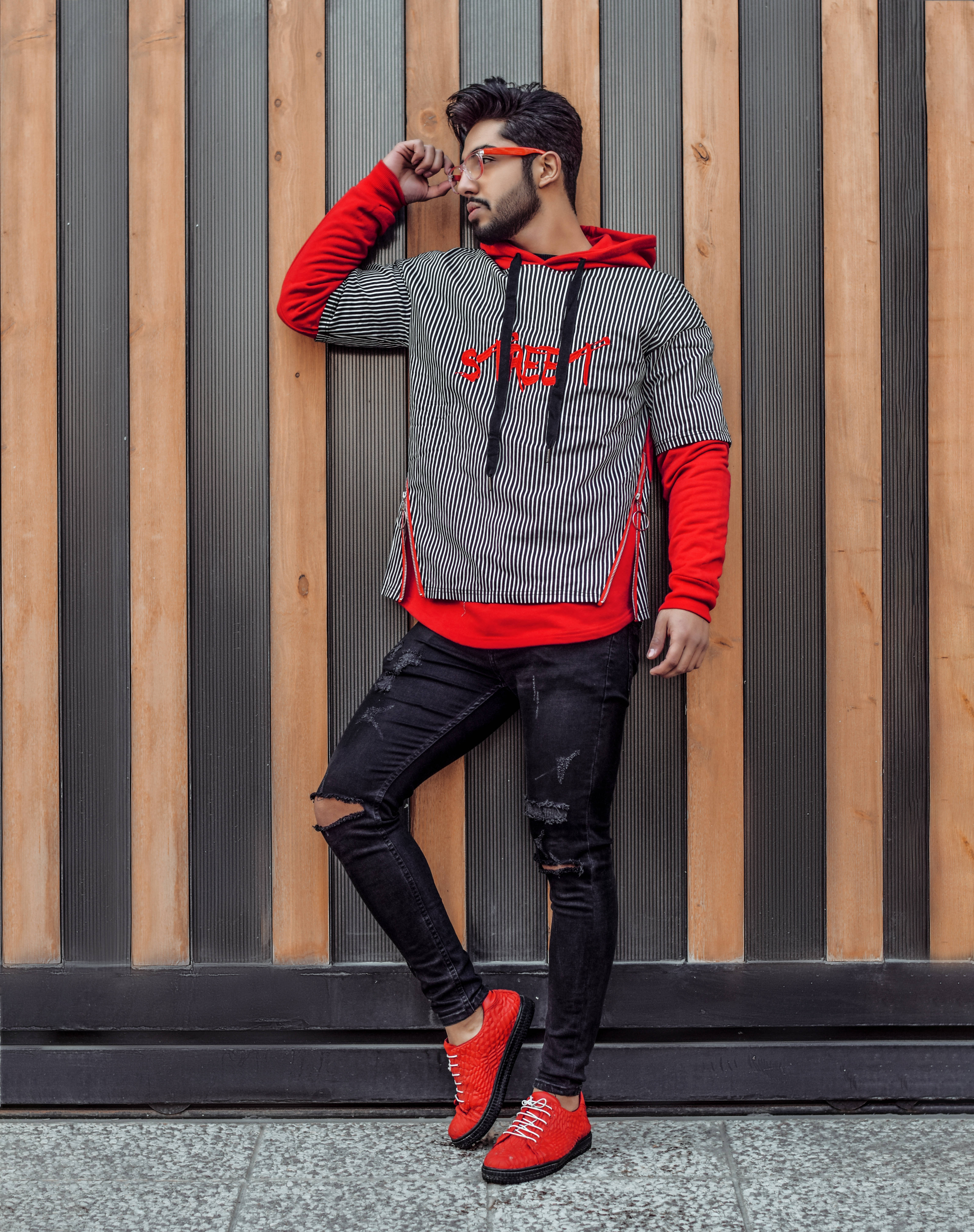 Trendy 桌布 壁紙 — 一位時尚男士穿著紅色運動鞋和條紋連帽衫，靠在木質和金屬牆上。