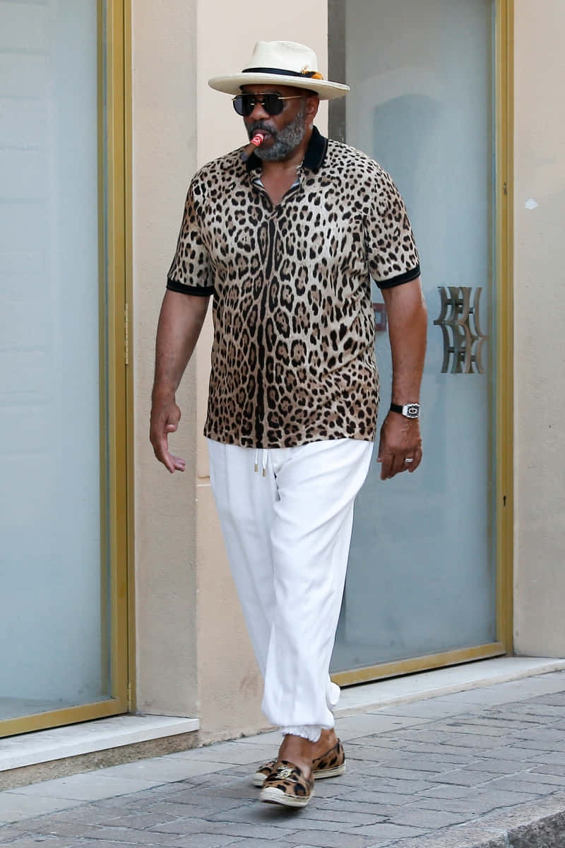 Celebrity 桌布 壁紙 — 一位時尚男士穿著豹紋襯衫和白色長褲，自信地走在陽光普照的城市人行道上。