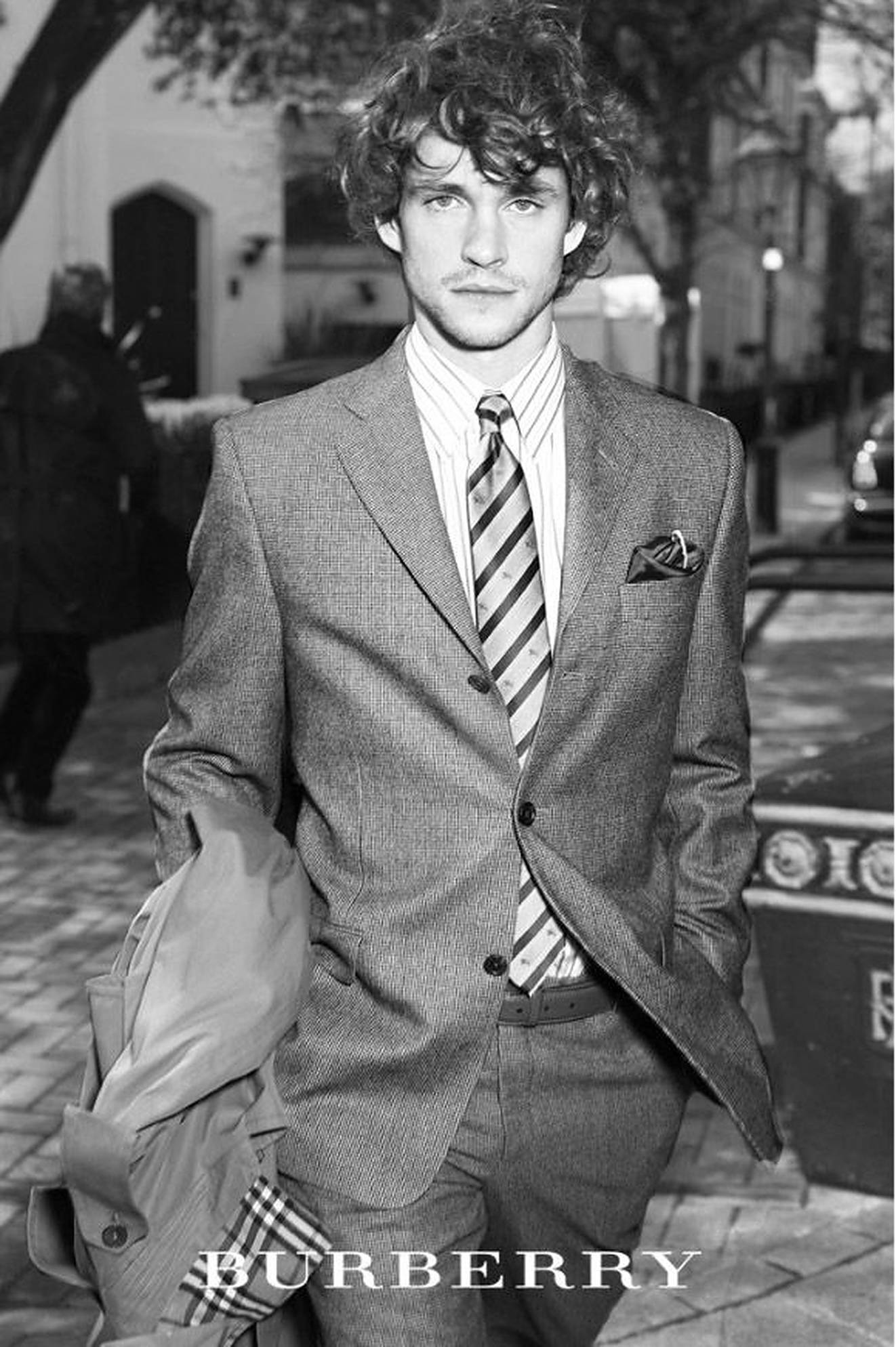 Hugh Dancy 桌布 壁紙 — 一位時尚男士穿著質感西裝和條紋領帶，自信地站在鵝卵石街道上，黑白風格。