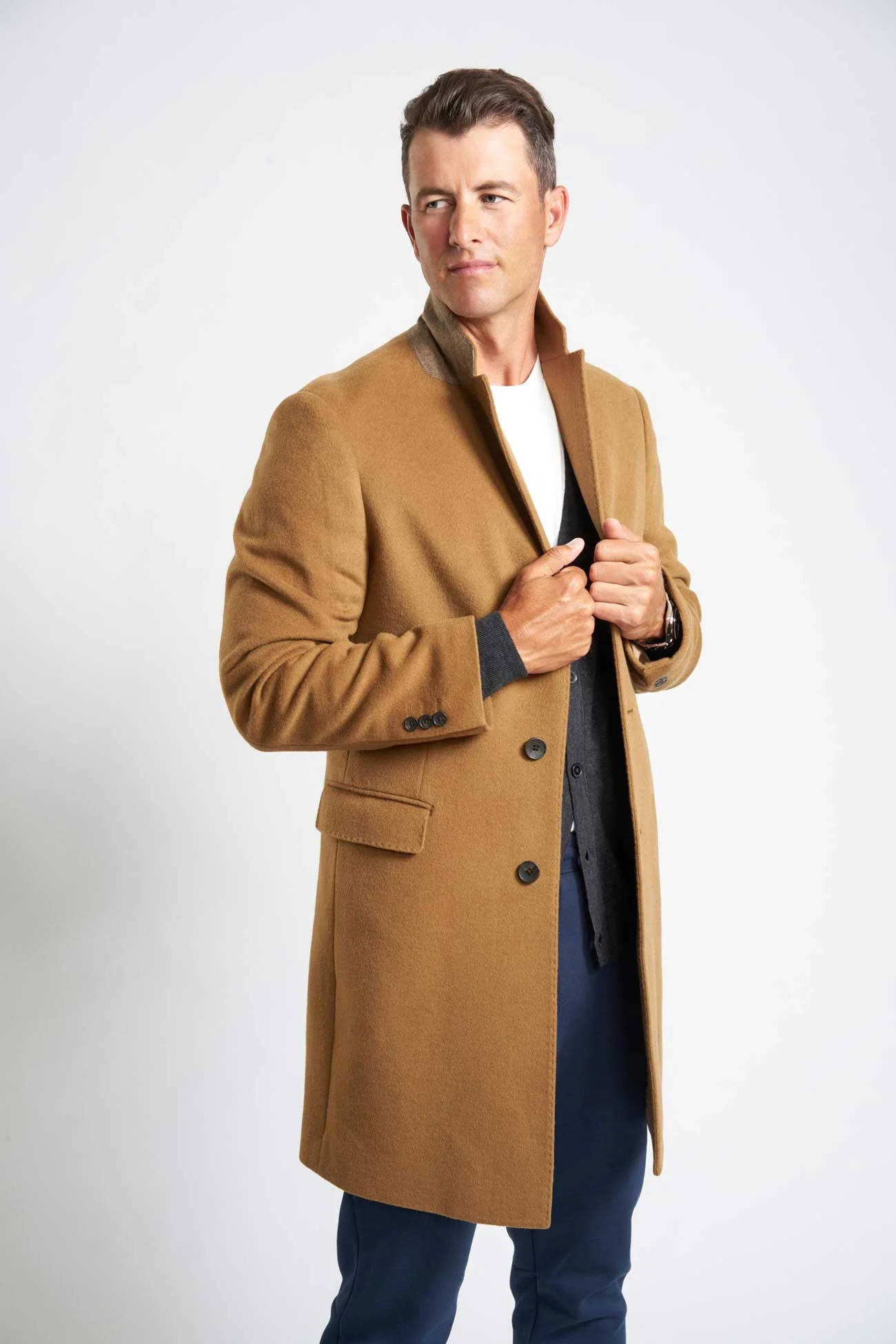 adam scott 桌布 壁紙 — 一位時尚男士穿著駝色大衣，在純白背景前自信地扣上外套鈕扣。