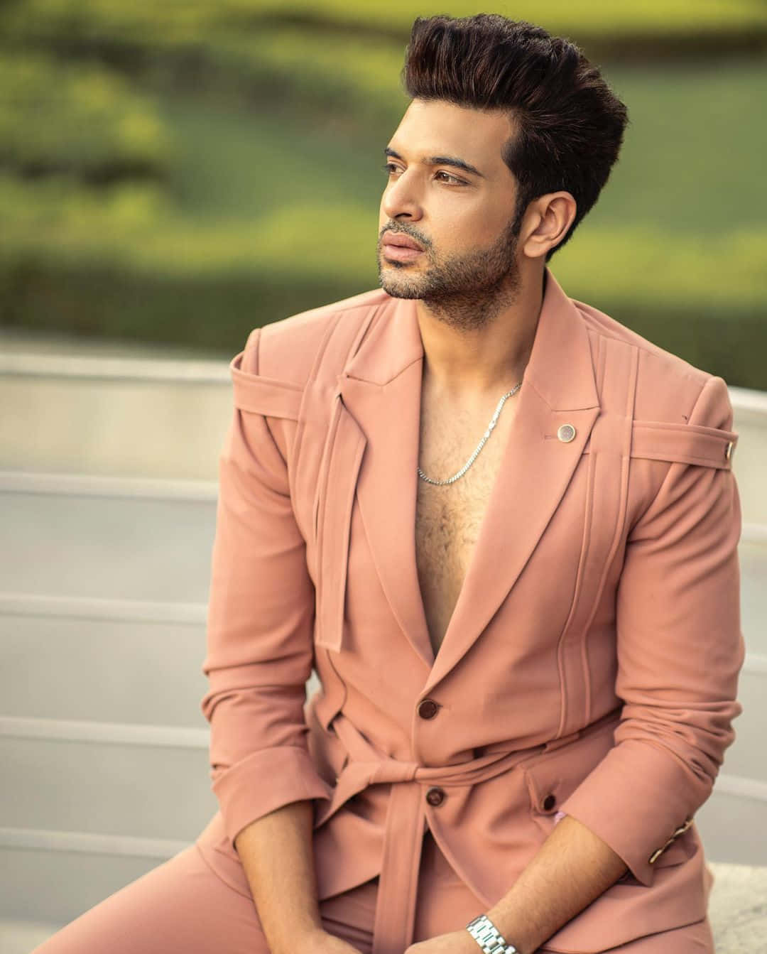 Dapper 桌布 壁紙 — 一位時尚男士身穿桃色西裝，坐在戶外，眼神若有所思，背景是模糊的綠色。