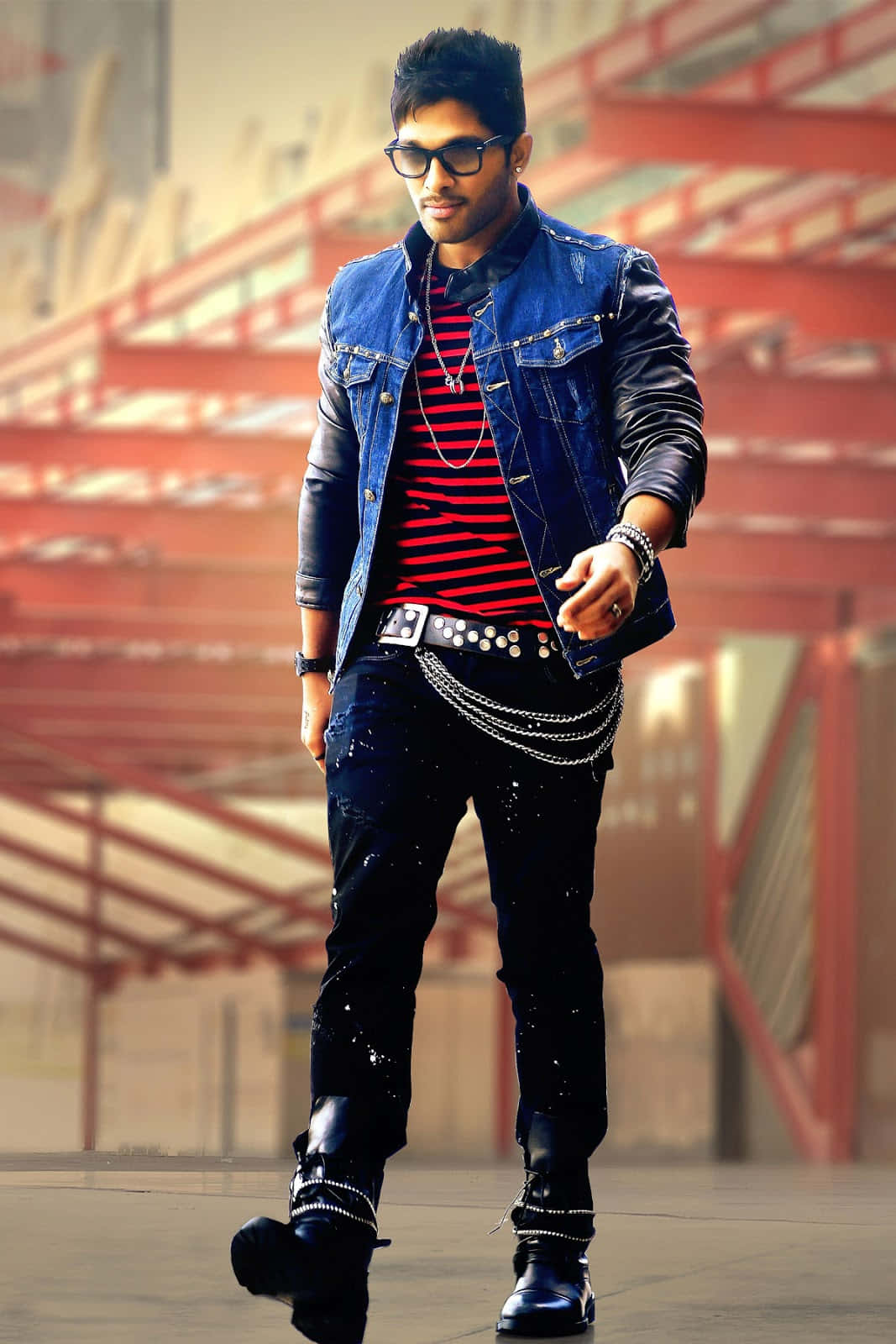 Allu Arjun 桌布 壁紙 — 一位時尚男士身穿牛仔外套和紅色條紋襯衫，在模糊的紅色工業結構前自信地擺姿勢。