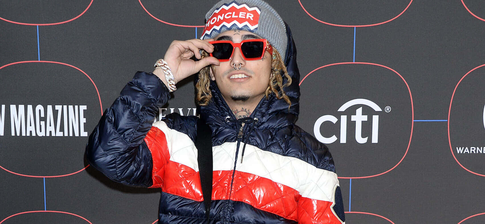 桌布 壁紙 — 一位時尚男士身穿紅白藍三色 Moncler 羽絨外套，在品牌活動背景下調整他的紅色太陽眼鏡。