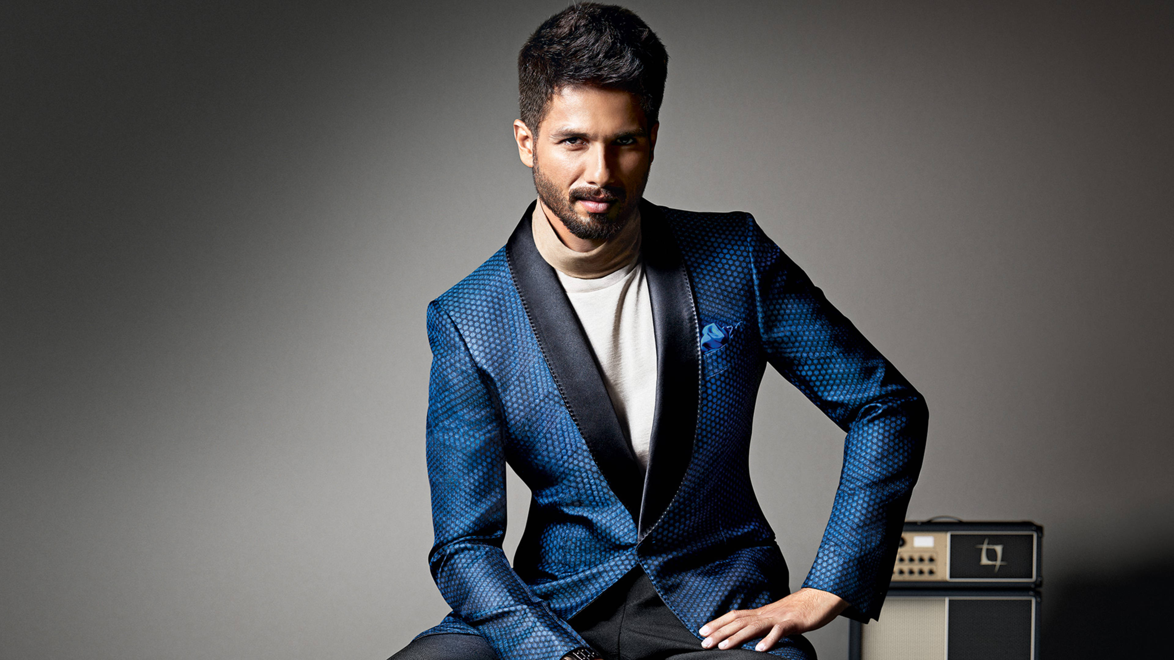 Shahid Kapoor 桌布 壁紙 — 一位時尚男士身穿藍色圖案燕尾服外套，在灰色攝影棚背景前自信擺姿勢，身旁放著一台復古擴音器。