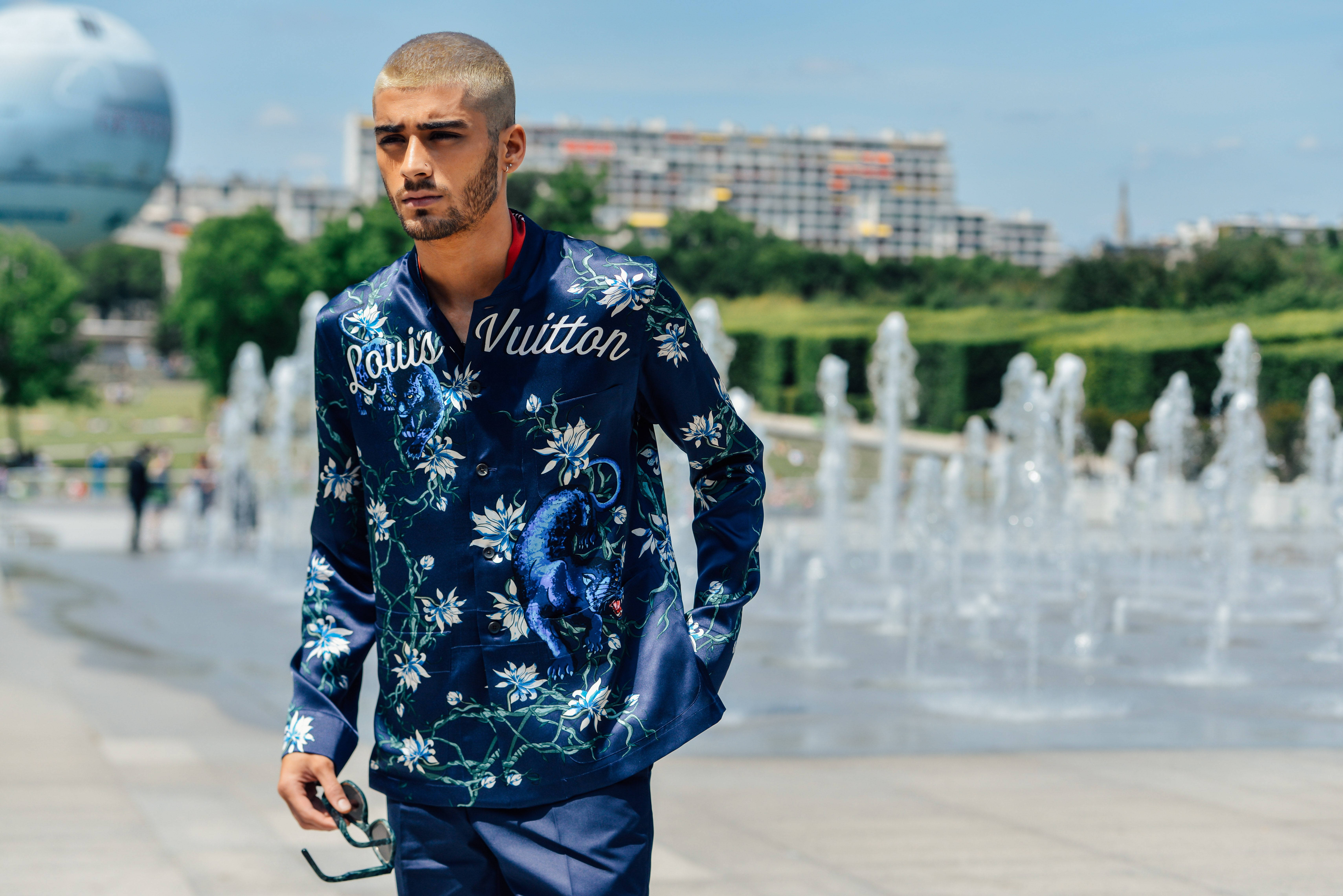 zayn 桌布 壁紙 — 一位時尚男士身穿藍色花卉圖案 Louis Vuitton 外套，在明亮的日光下自信地站在噴泉附近。