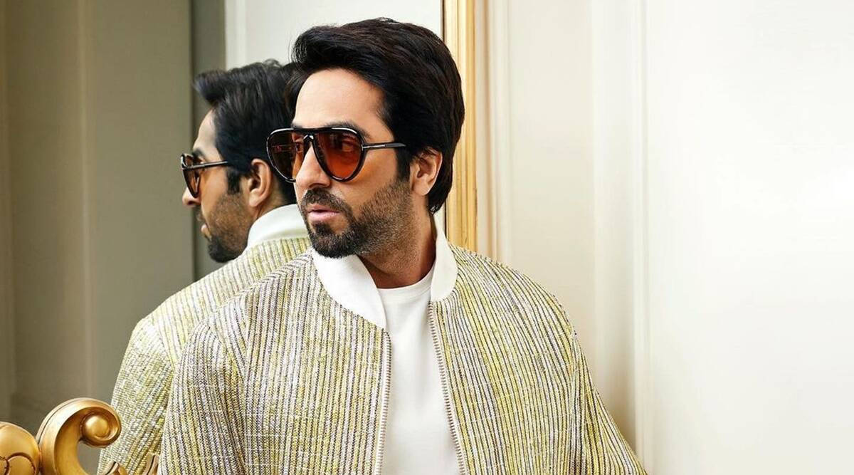 ayushmann khurrana 桌布 壁紙 — 一位時尚男士身穿金色條紋外套和太陽眼鏡，站在豪華室內的鏡子前。