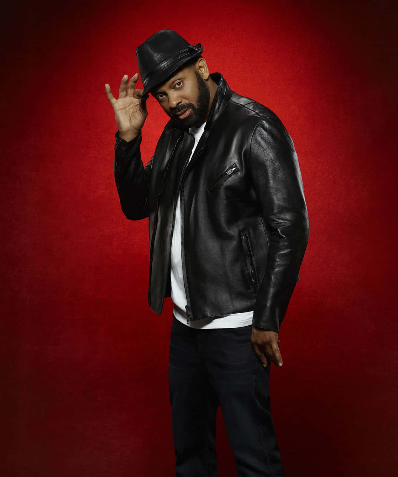 Mike Epps 桌布 壁紙 — 一位時尚男士身穿黑色皮夾克和紳士帽，在豐富的紅色紋理背景前自信地擺姿勢。