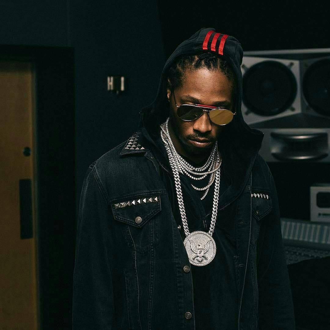 90s Rapper 桌布 壁紙 — 一位時尚男士身穿黑色連帽衫和牛仔外套，飾有銀鏈和大獎章，站在身後有揚聲器的昏暗錄音室中。
