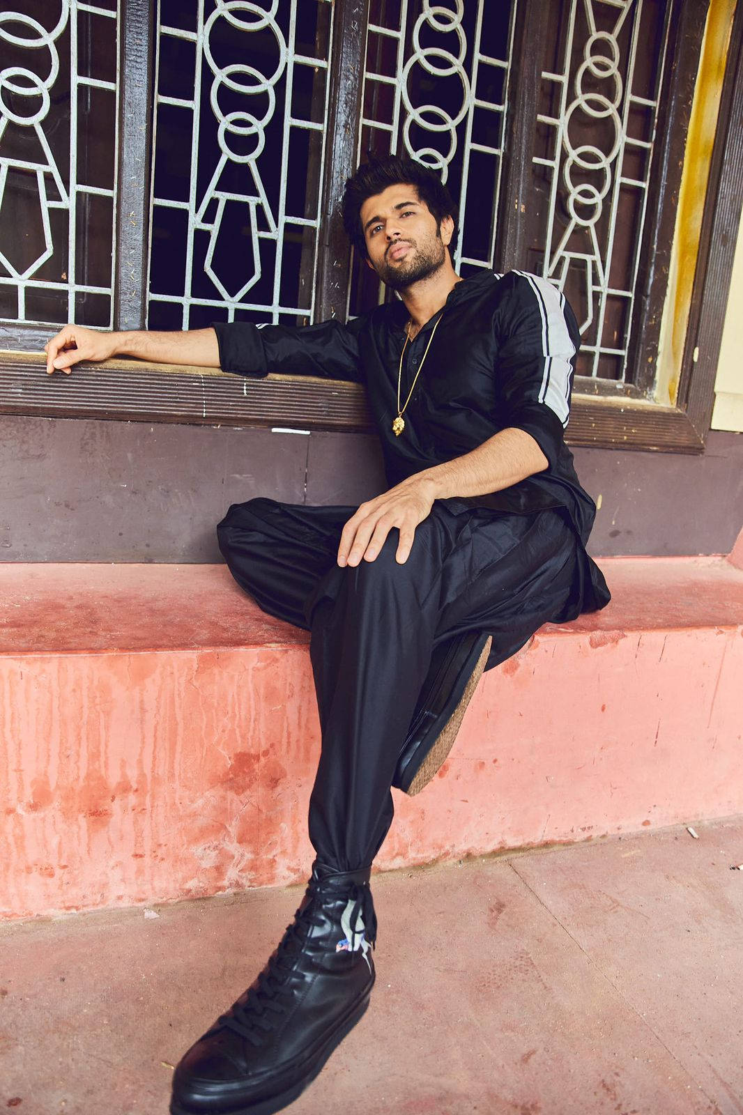 Indian 桌布 壁紙 — 一位時尚男士身穿黑色運動服，自信地靠在粉紅色混凝土台階上，背景是華麗的金屬窗格柵。