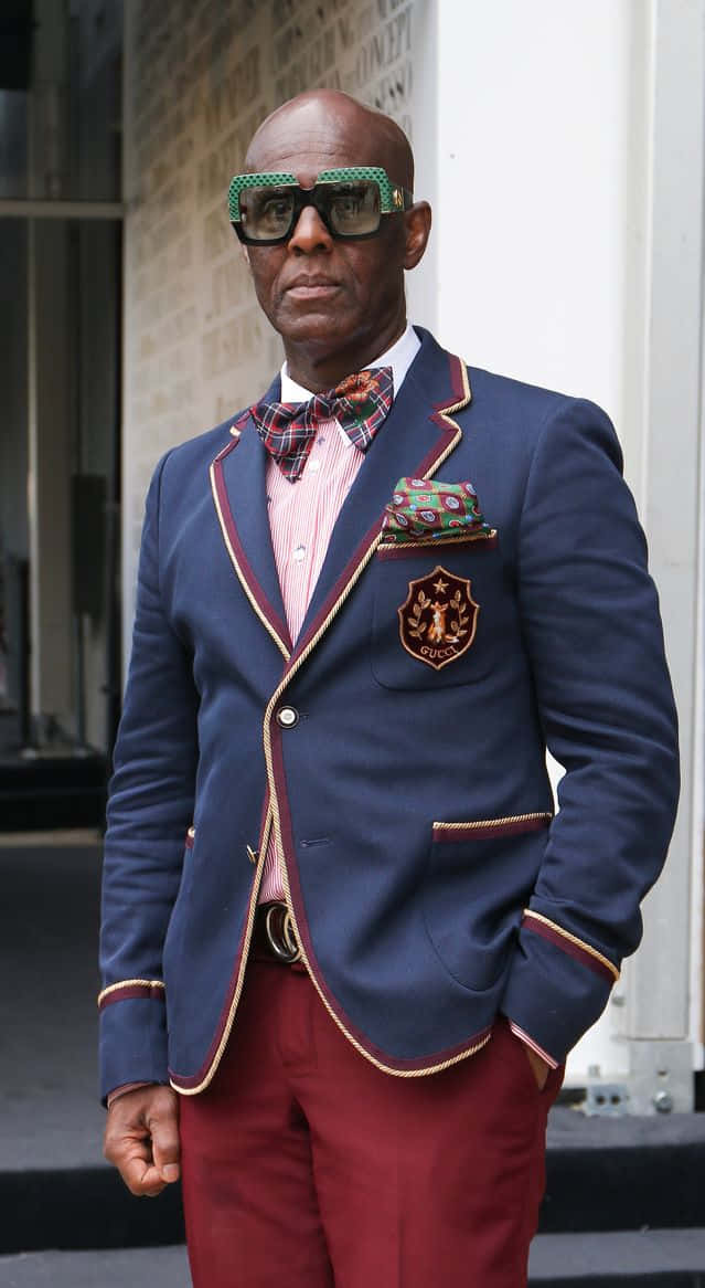 Dapper 桌布 壁紙 — 一位時尚的光頭男士穿著海軍藍西裝外套，帶紅色飾邊和圖案領結，自信地站在城市人行道上。