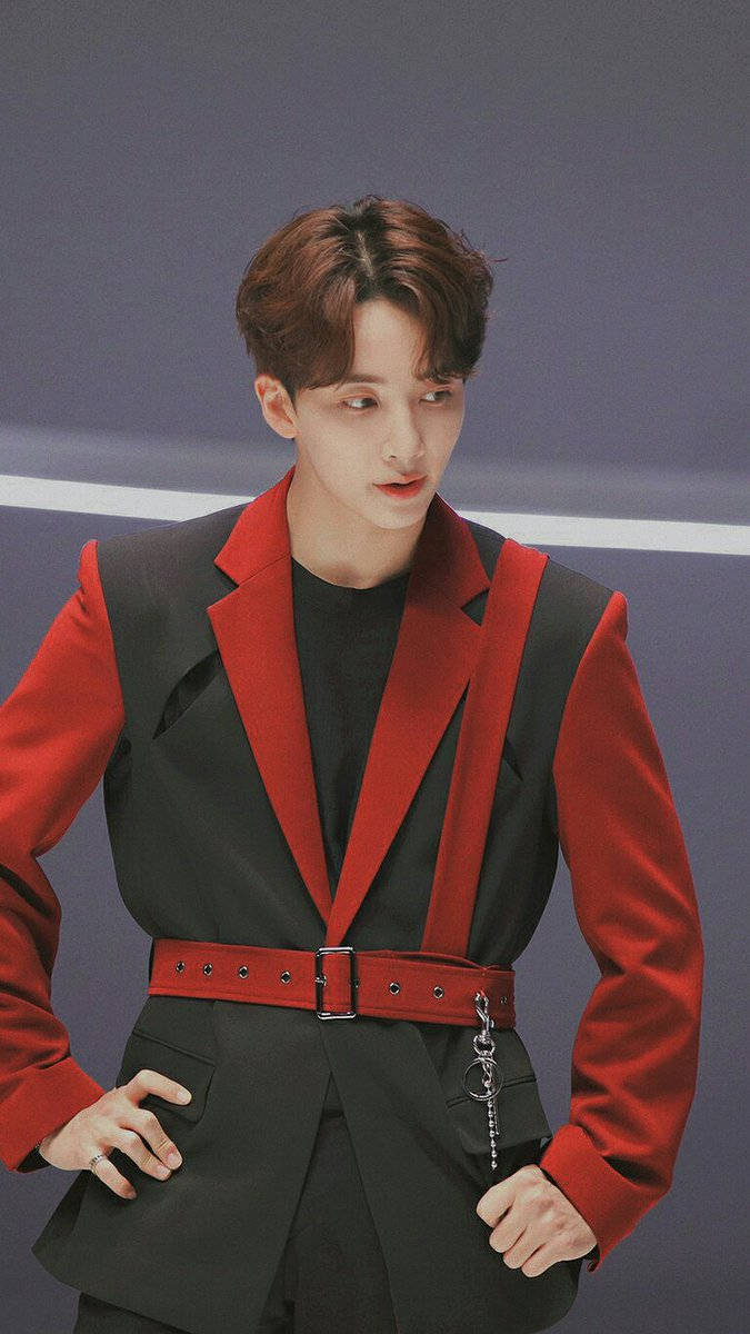yoon jeonghan 桌布 壁紙 — 一位時尚的年輕男士穿著大膽的紅黑西裝，在簡約的灰色背景前自信地擺姿勢。