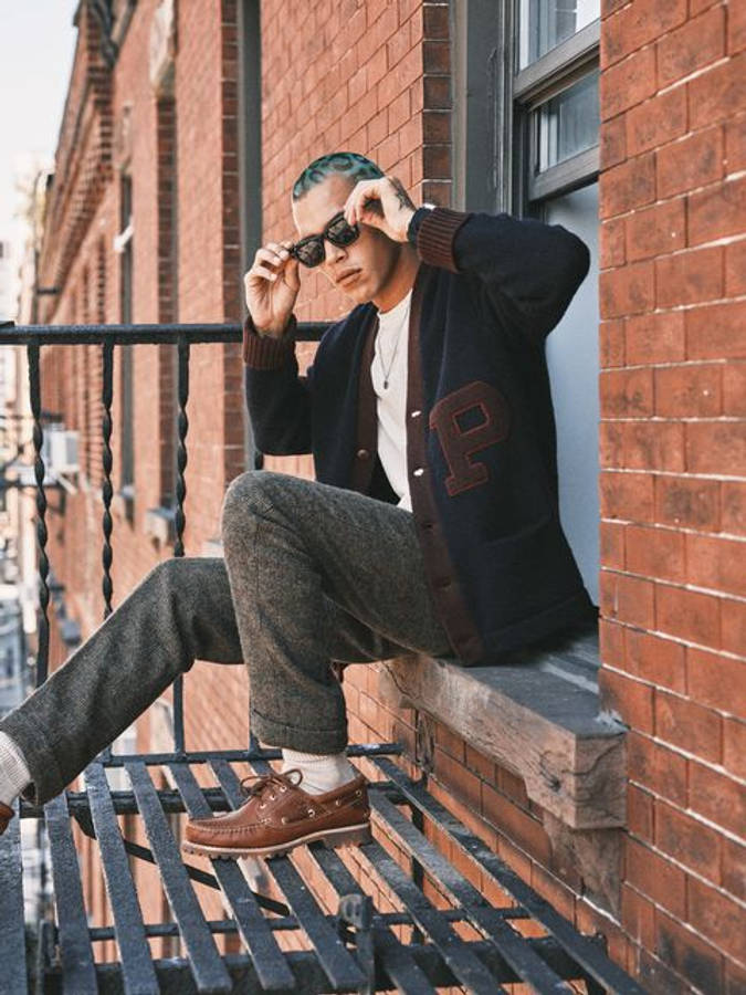 ralph lauren 桌布 壁紙 — 一位時尚的年輕男子，頭髮帶有藍色調，坐在紅磚牆前的防火梯上，隨意地調整太陽眼鏡。