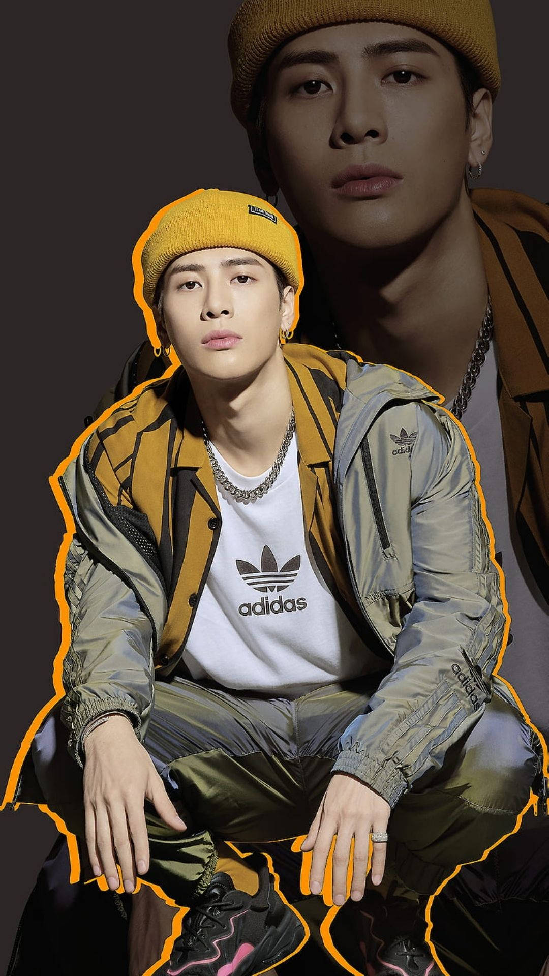 王嘉爾 桌布 壁紙 — 一位時尚的年輕男子戴著黃色毛帽和Adidas外套，在深色背景前自信地擺姿勢，帶有發光的橙色輪廓。