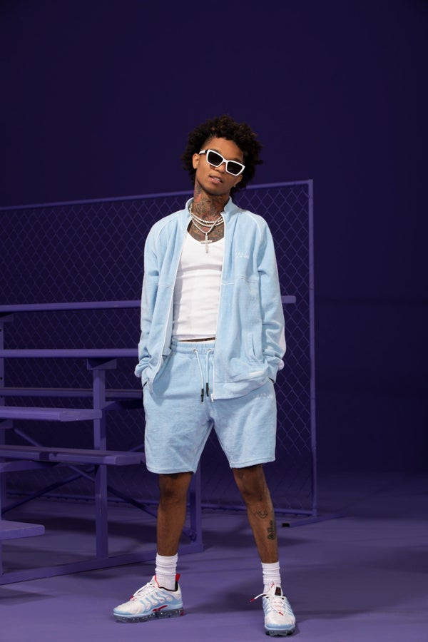 Swae Lee 桌布 壁紙 — 一位時尚的年輕男子穿著淺藍色運動衫和白色太陽眼鏡，在紫色鐵絲網背景前自信地擺姿勢。