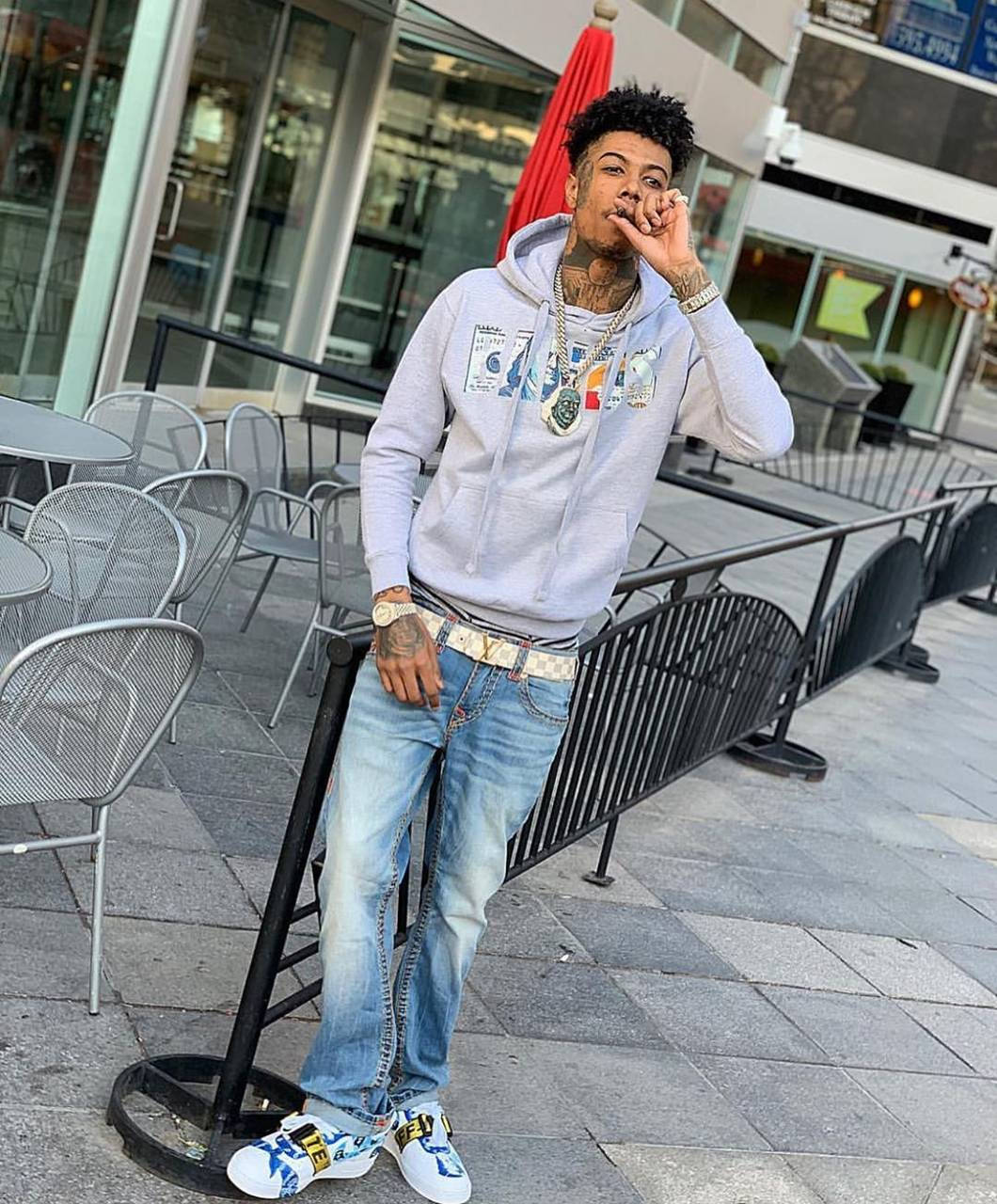Celebrity 桌布 壁紙 — 一位時尚的年輕男子穿著灰色連帽衫和藍色牛仔褲，隨意地靠在戶外的欄杆上抽煙。