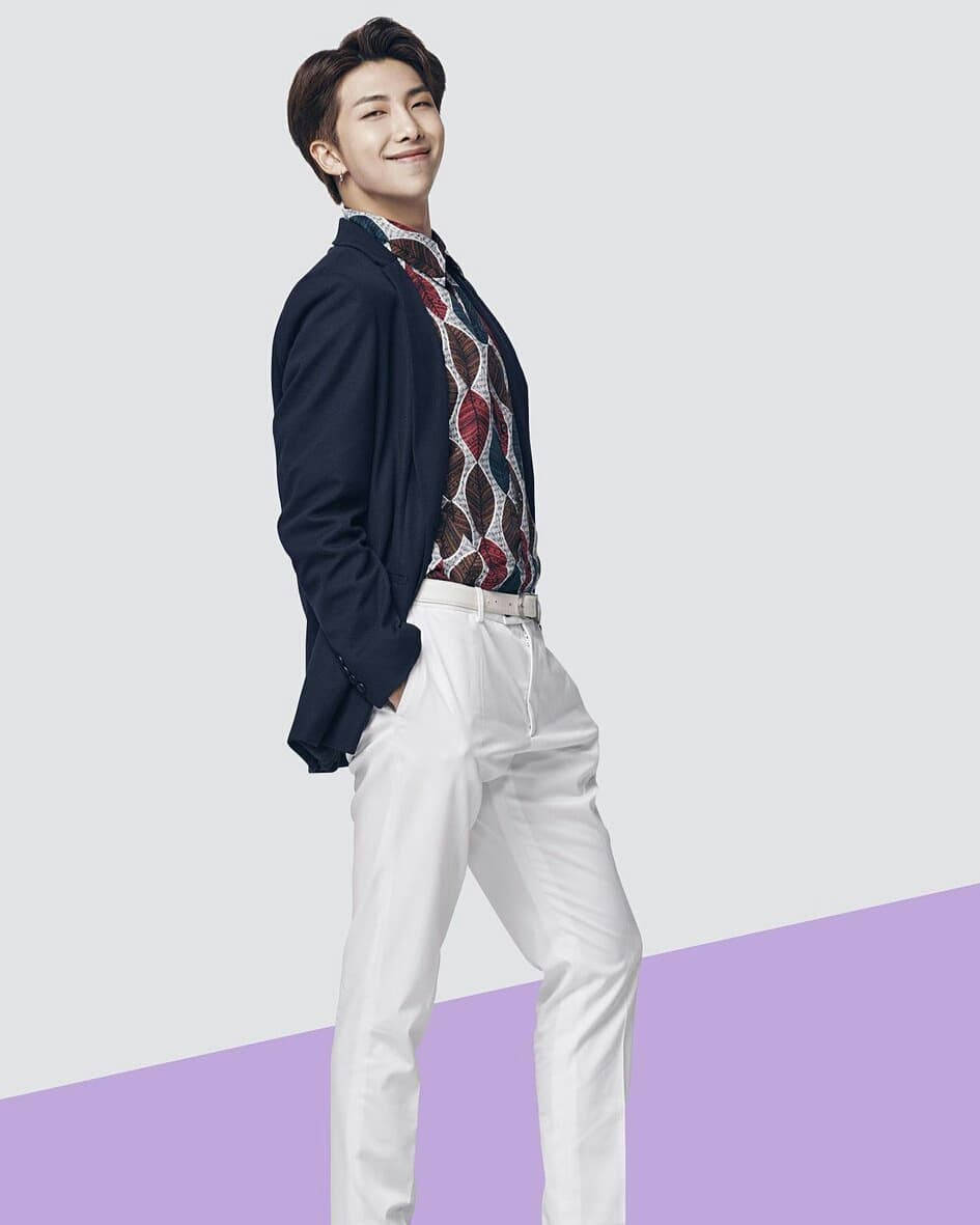 Namjoon 桌布 壁紙 — 一位時尚的年輕男子身穿海軍藍西裝外套和白色長褲，在簡約的紫色和灰色背景前自信地擺姿勢。