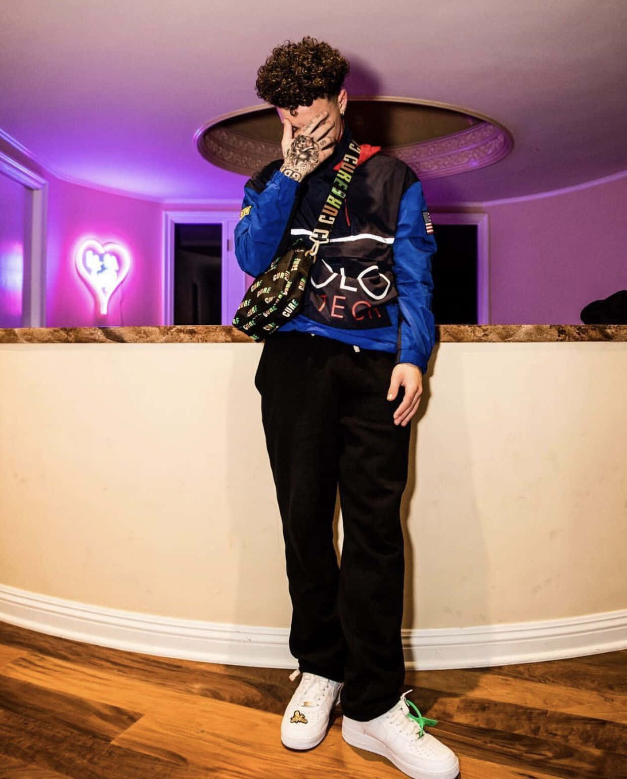 Lil Mosey 桌布 壁紙 — 一位時尚的年輕男子身穿藍色外套和白色運動鞋，在一個帶有心形標誌的紫色霓虹燈房間裡擺姿勢。