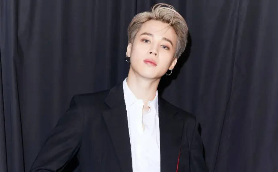 BTS 智旻 桌布 壁紙 — 一位時尚的年輕金髮男子戴著圓環耳環，穿著黑色西裝在深色窗簾背景下自信地擺姿勢。