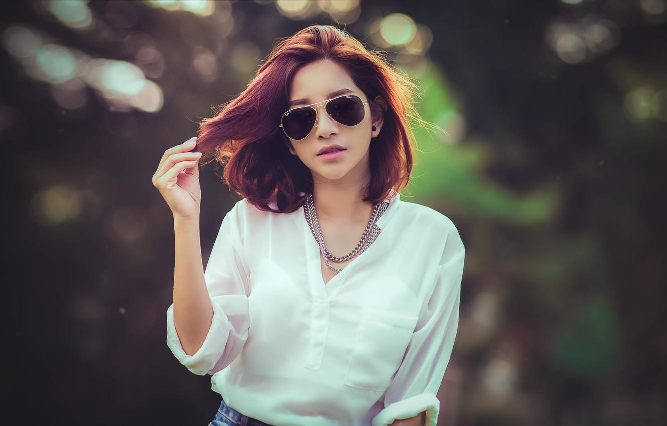 Thailand Woman 桌布 壁紙 — 一位時尚的紅髮女性戴著太陽眼鏡，穿著白色襯衫在戶外擺姿勢，背景是模糊的綠色。