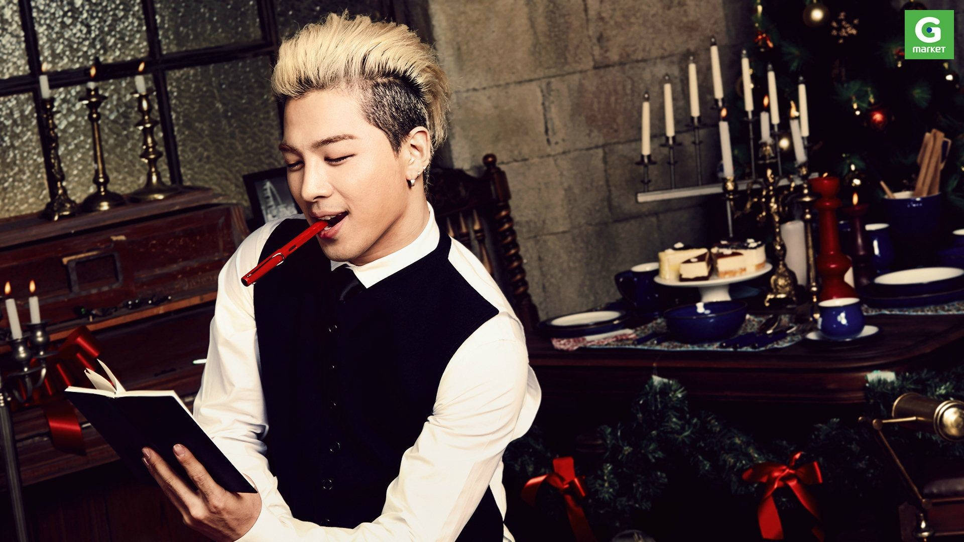 Bigbang 桌布 壁紙 — 一位時尚的金髮男子拿著一本書和一支紅色筆，坐在一個裝飾著聖誕節的節日燭光房間裡。