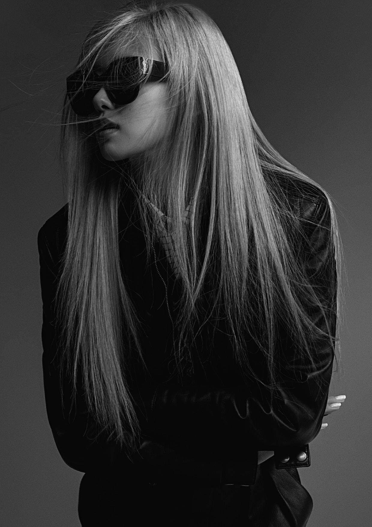 Sunglasses 桌布 壁紙 — 一位時尚的長髮金髮女子戴著太陽眼鏡，穿著黑色皮夾克，在純灰色背景前擺姿勢。