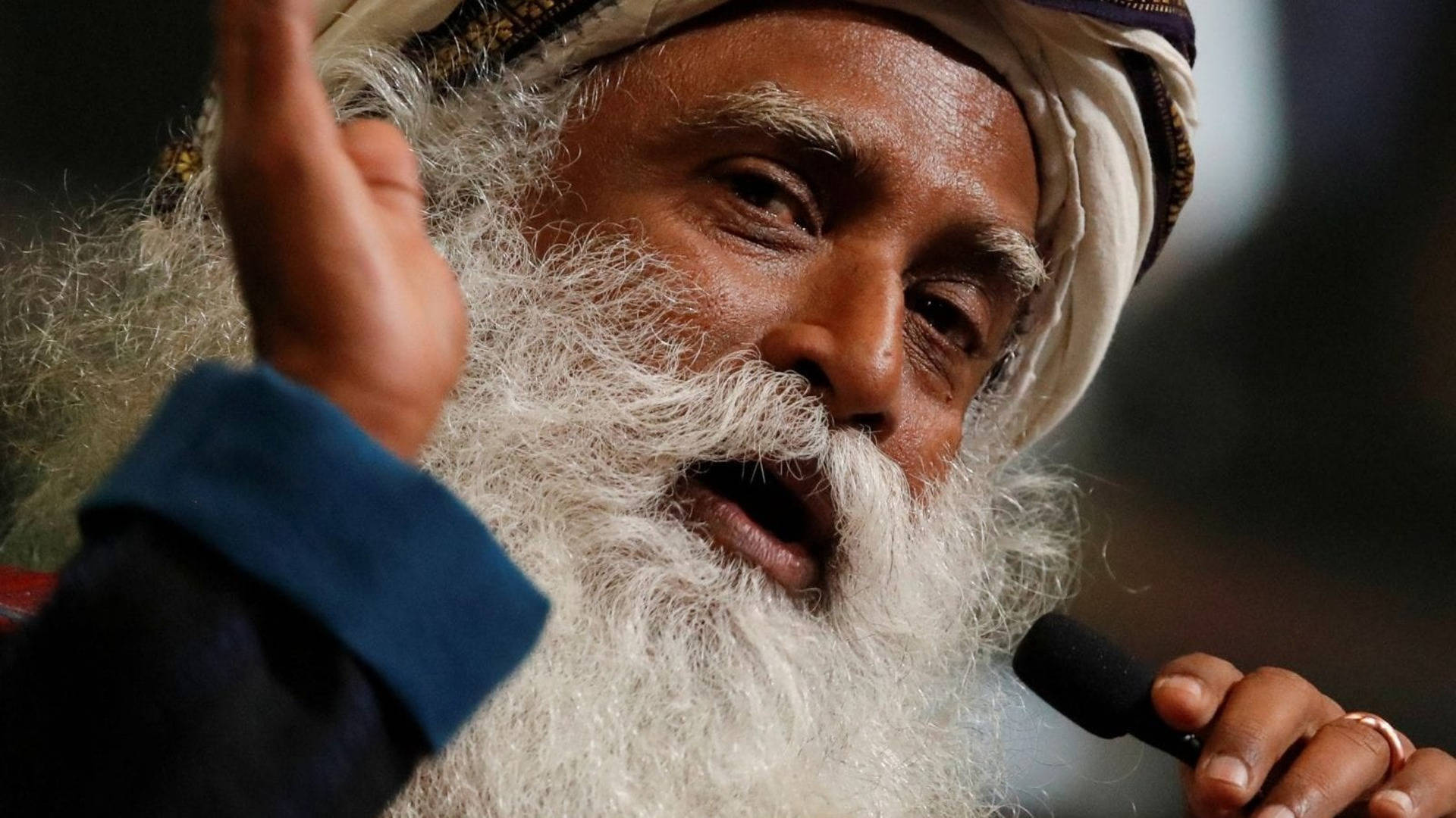 Indian 桌布 壁紙 — 一位智慧長者留著長長的白鬍子，對著麥克風激情演講，同時舉起手做手勢的特寫。