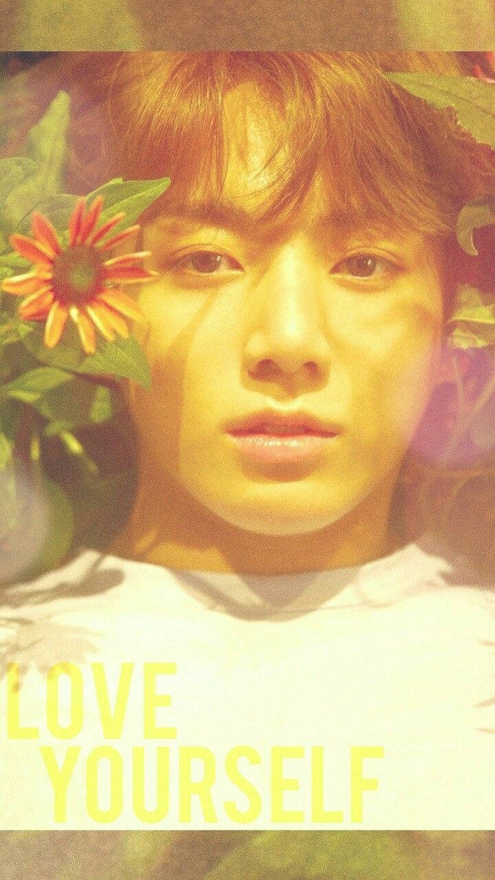 Jungkook 桌布 壁紙 — 一位暖色調頭髮的年輕男子在金色陽光下，被綠葉和鮮豔的橙色花朵環繞，溫柔地凝視著。
