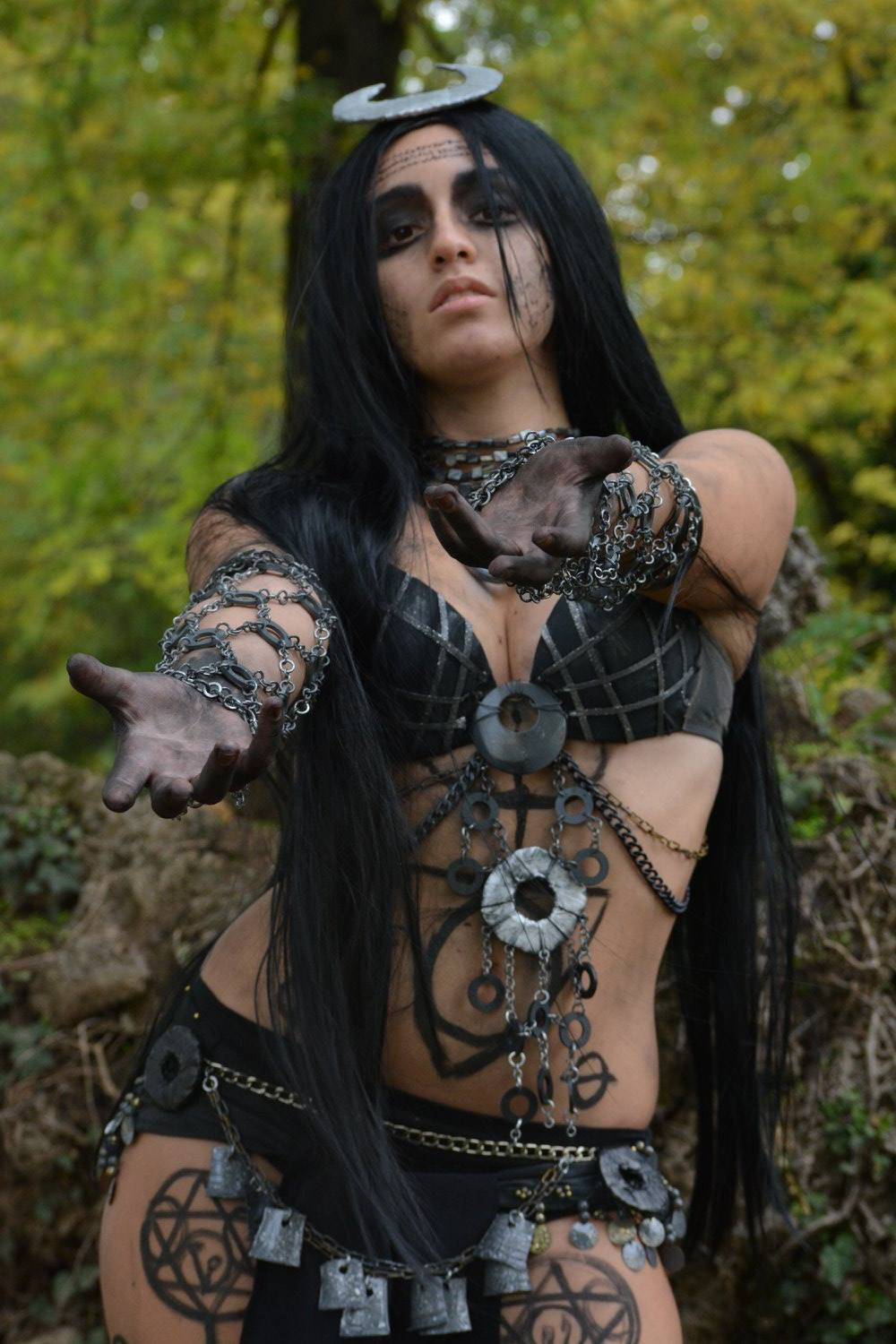 Enchantress 桌布 壁紙 — 一位暗黑裝扮的長黑髮女子，帶著鎖鏈，在森林中伸出雙手。