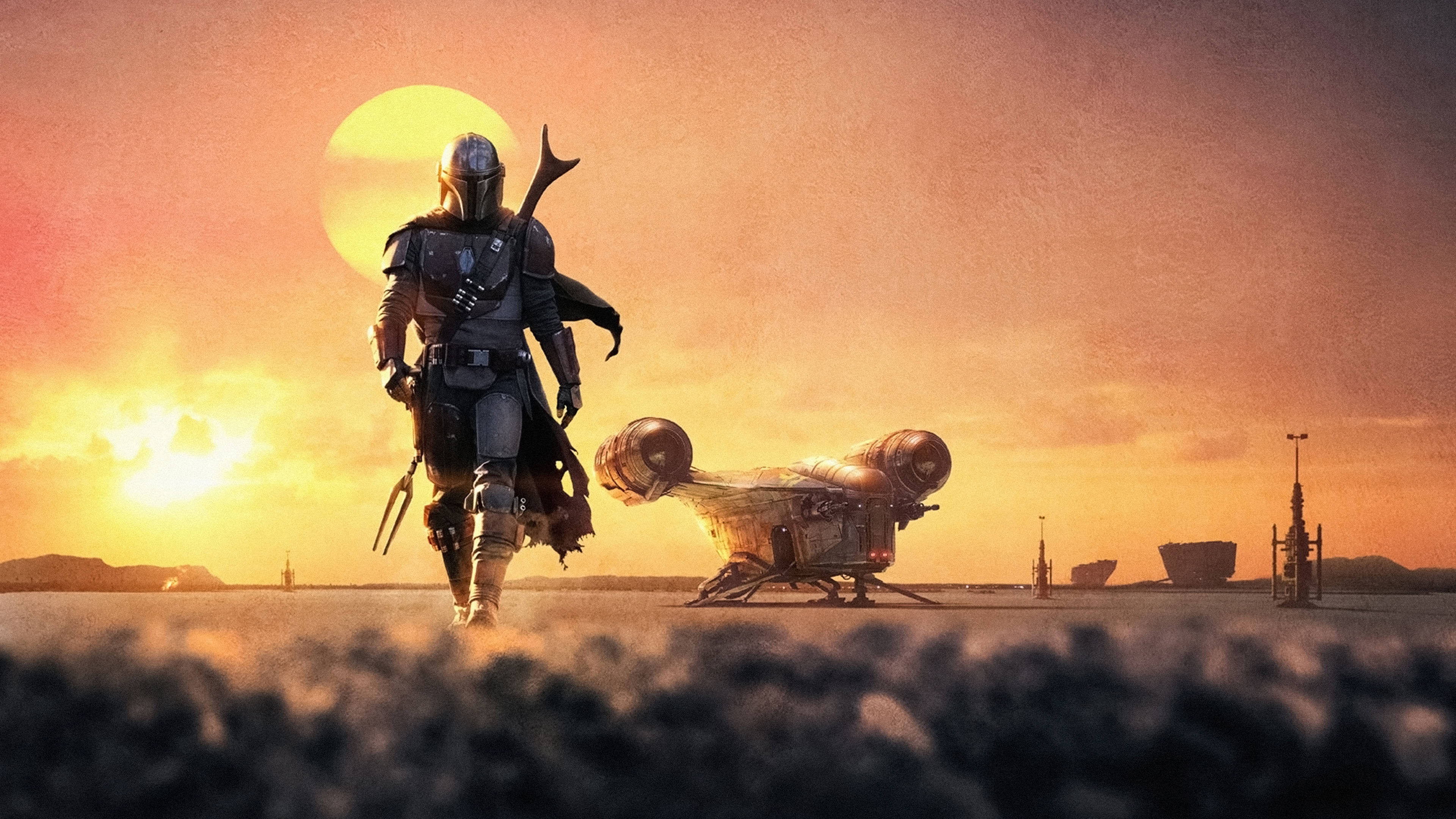 Mandalorian 桌布 壁紙 — 一位曼達洛戰士在日落時分穿越沙漠，走在他墜毀的星際飛船旁邊，身後有一顆巨大的太陽。