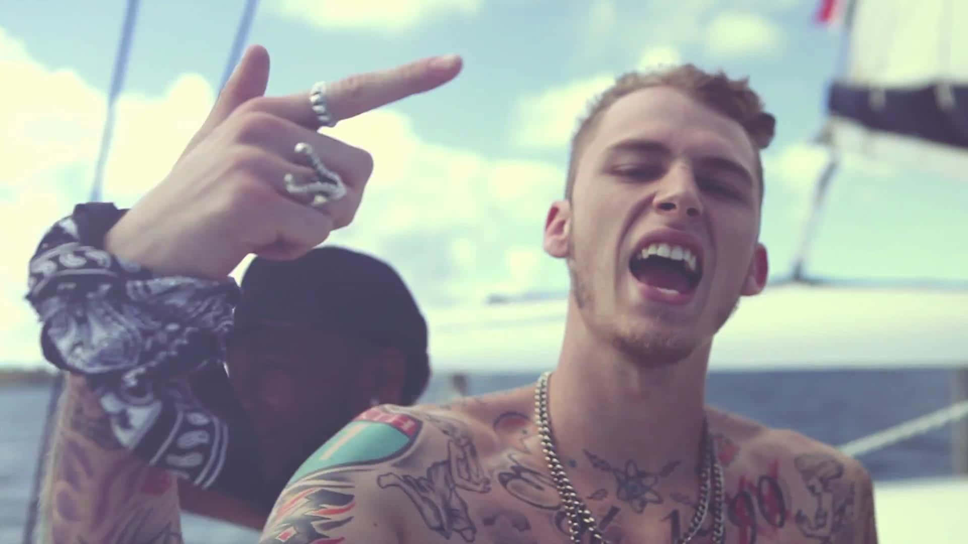mgk 桌布 壁紙 — 一位有刺青、戴銀戒指的男子在晴朗天空下的帆船上歡樂地呼喊。