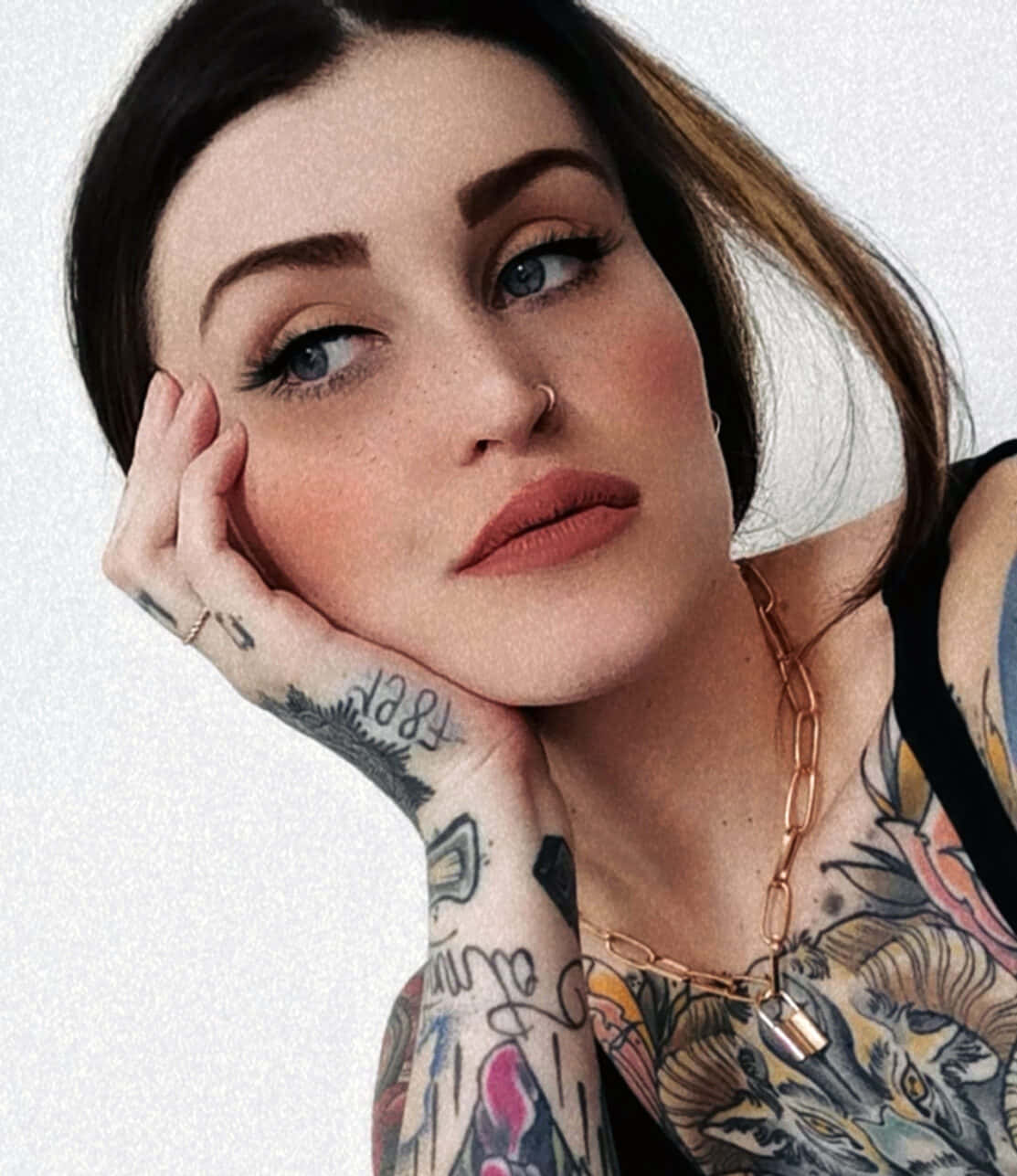 Tattoo Girl 桌布 壁紙 — 一位有刺青、藍眼睛的女性，在純白色背景上將下巴擱在手上。