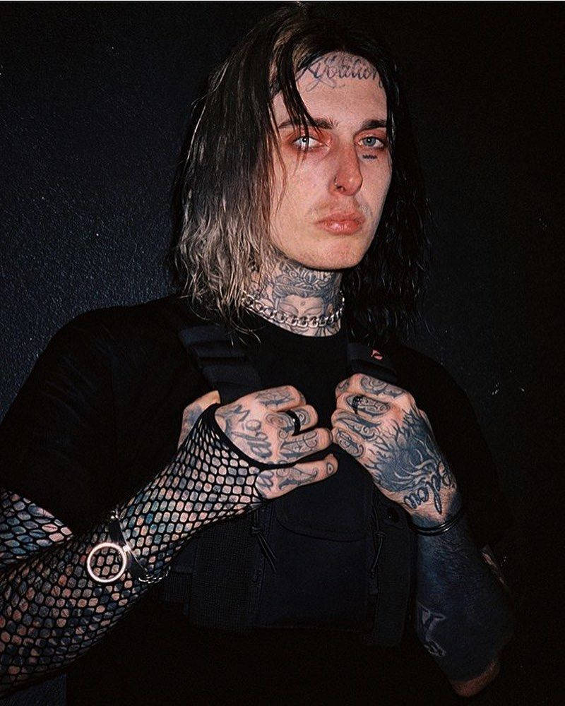 Ghostemane 桌布 壁紙 — 一位有刺青、長黑髮、戴魚網手套的人，穿著黑色背心在黑色背景前擺姿勢。