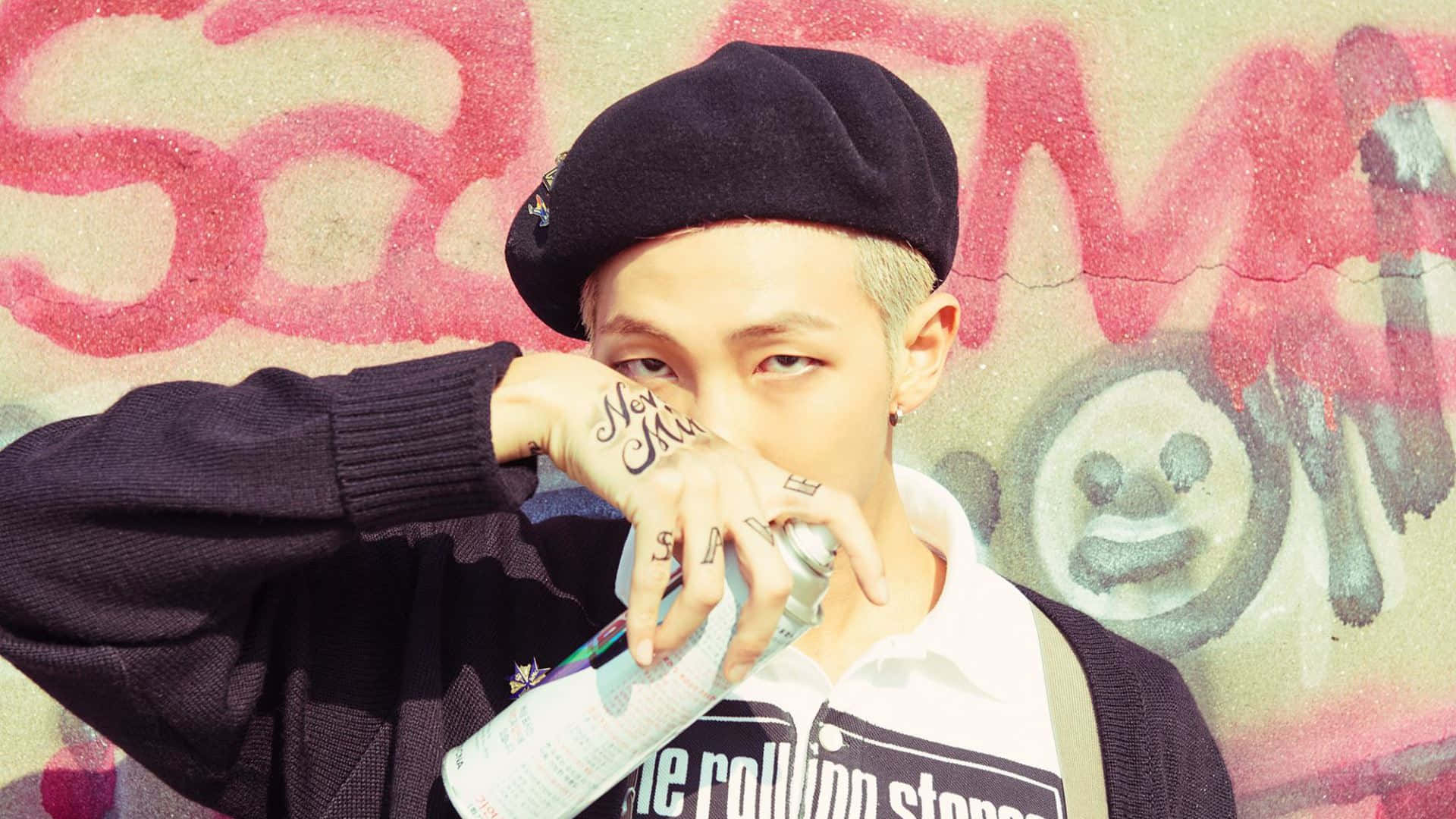 Bts Rap Monster 桌布 壁紙 — 一位有刺青並戴著貝雷帽的年輕人，在佈滿塗鴉的牆前拿著噴漆罐。