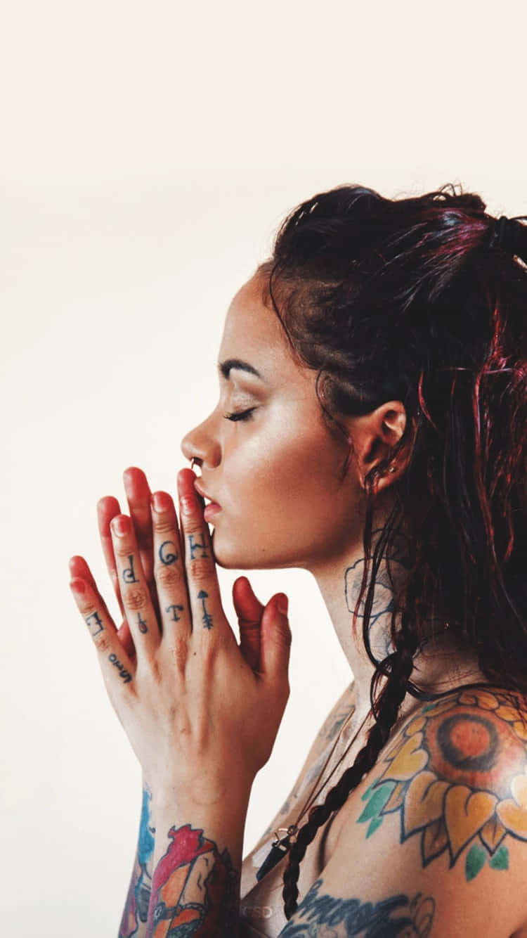 kehlani 桌布 壁紙 — 一位有刺青和辮子頭髮的女性，在純色背景前雙手合十祈禱。