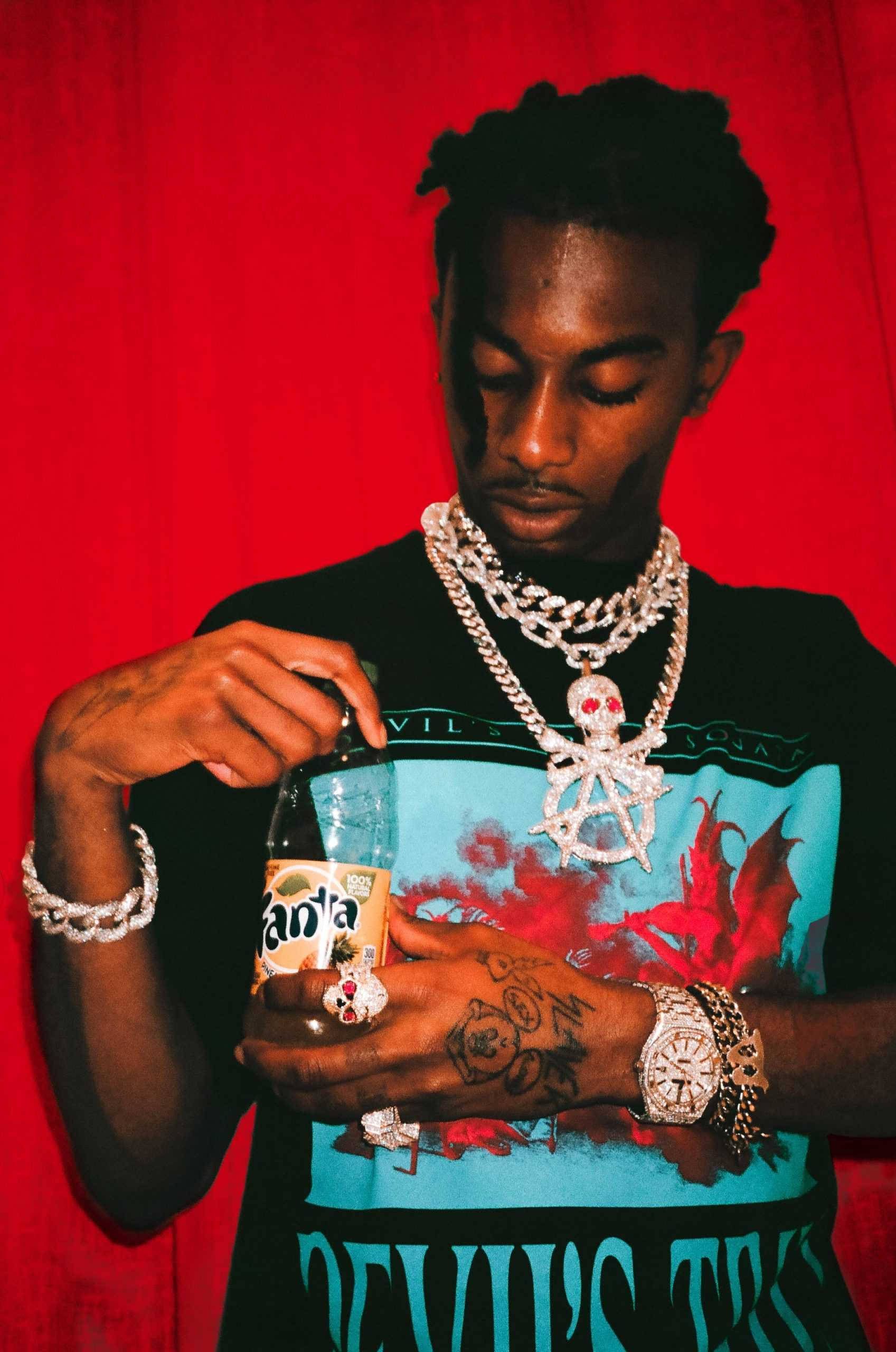 Carti 桌布 壁紙 — 一位有刺青和鑽石首飾的時尚男士在鮮紅色背景下打開芬達瓶。