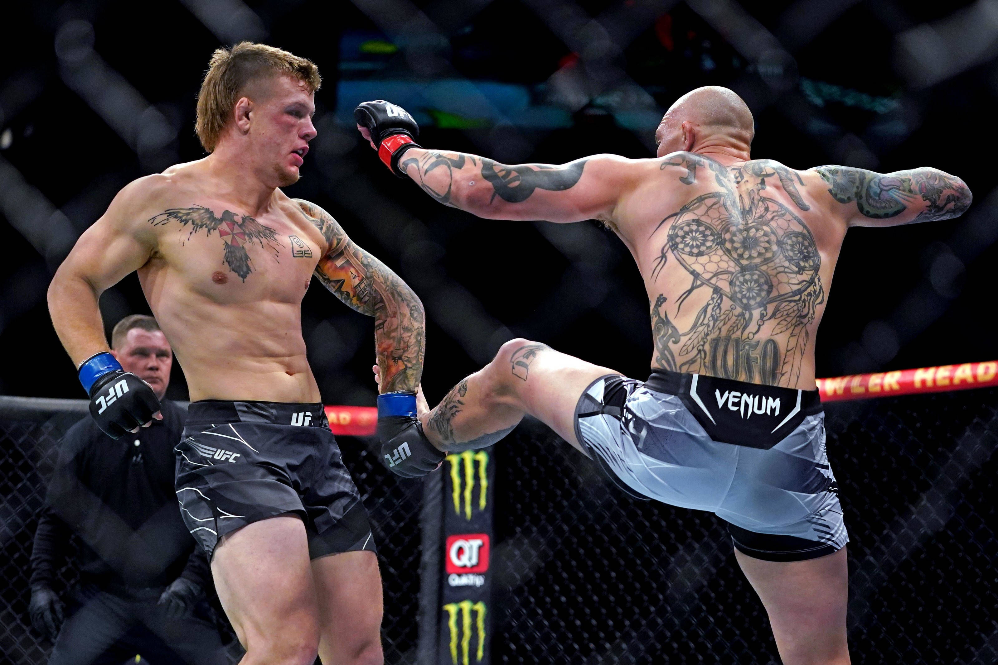 MMA 桌布 壁紙 — 一位有刺青的MMA拳手在明亮的場館燈光下，於UFC八角籠內向對手使出高踢。