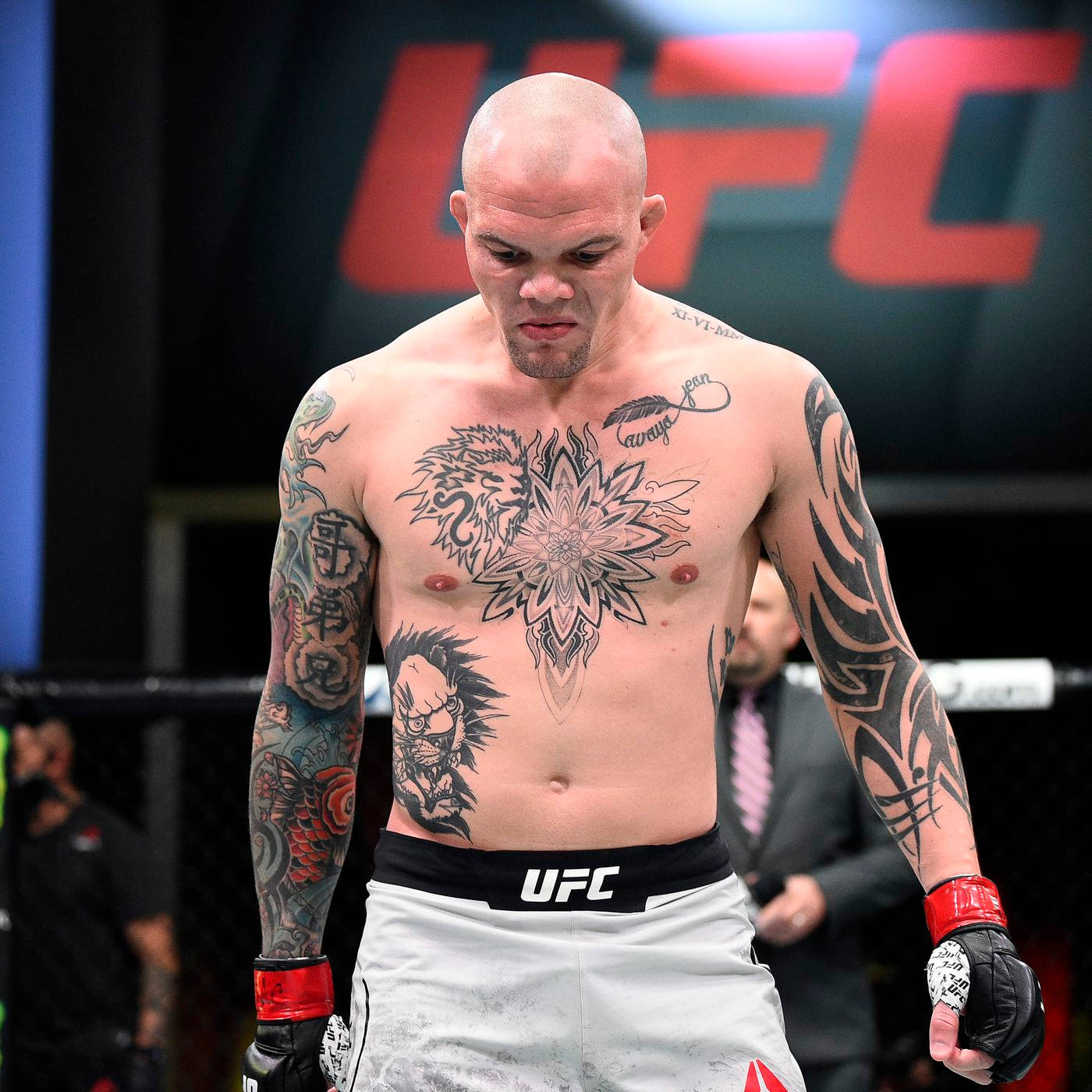MMA 桌布 壁紙 — 一位有刺青的UFC拳手，身穿白色短褲和紅色手套，帶著專注的表情站在八角籠中。